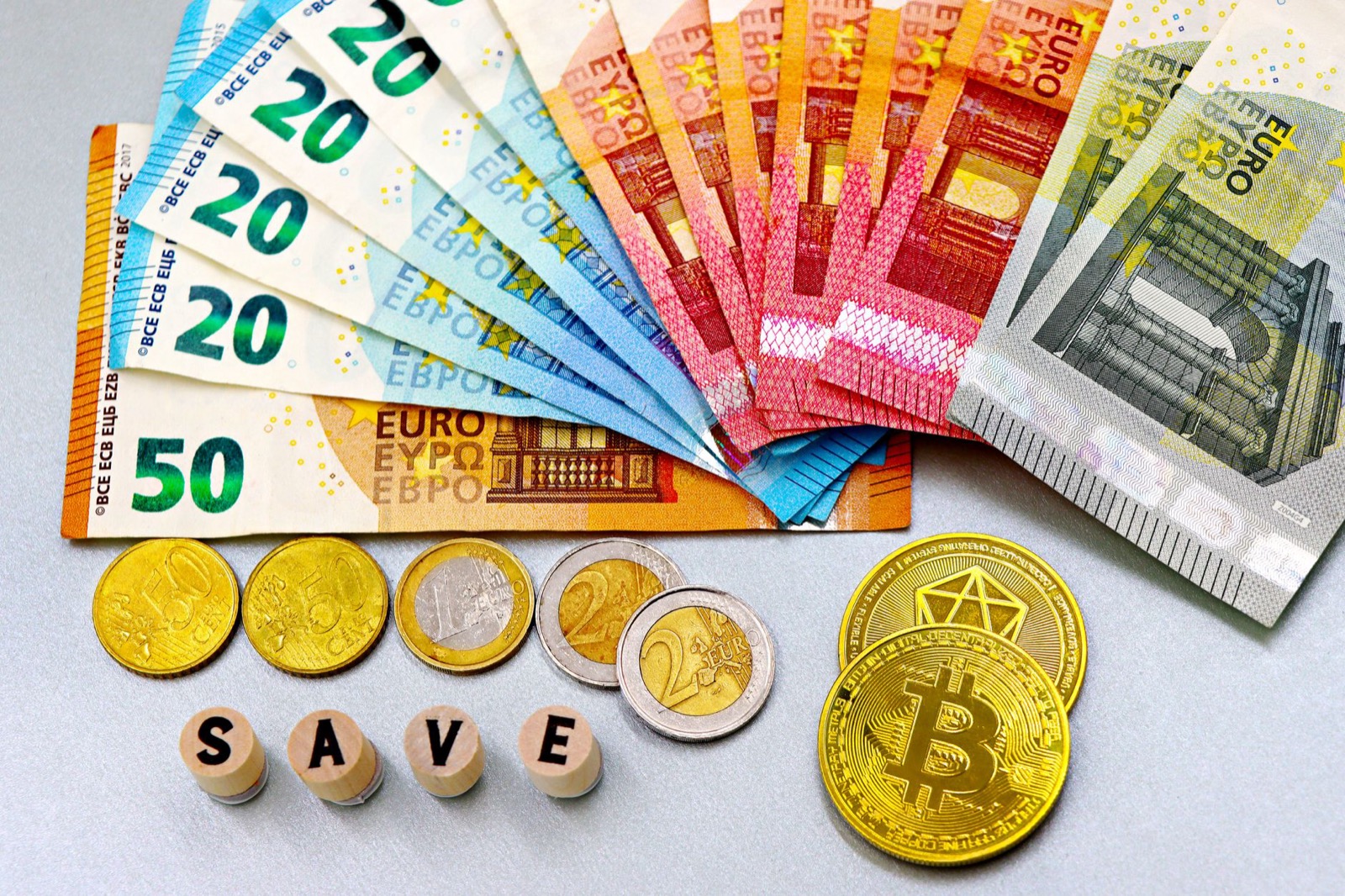 Euro banknotes fanned out with euro coins, letter blocks spelling SAVE and a gold novelty bitcoin