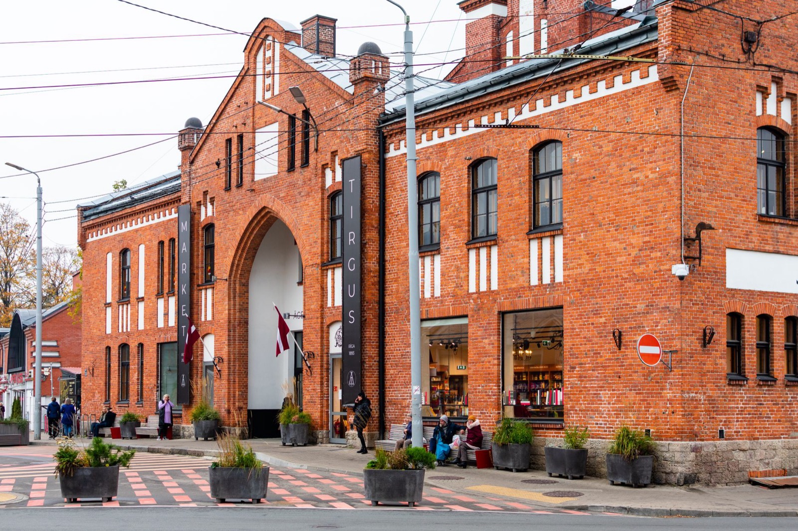 The red brick front of a market hall with a Tirgus banner and a Latvian flag