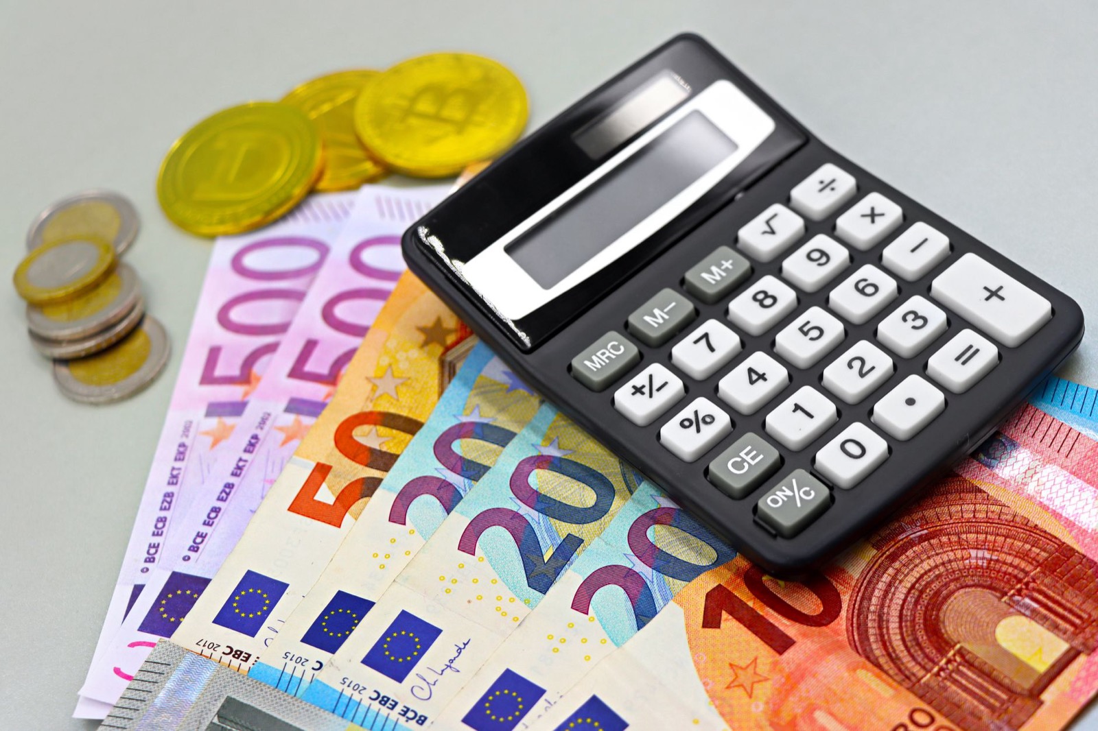 Euro banknotes and coins fanned out under a pocket calculator
