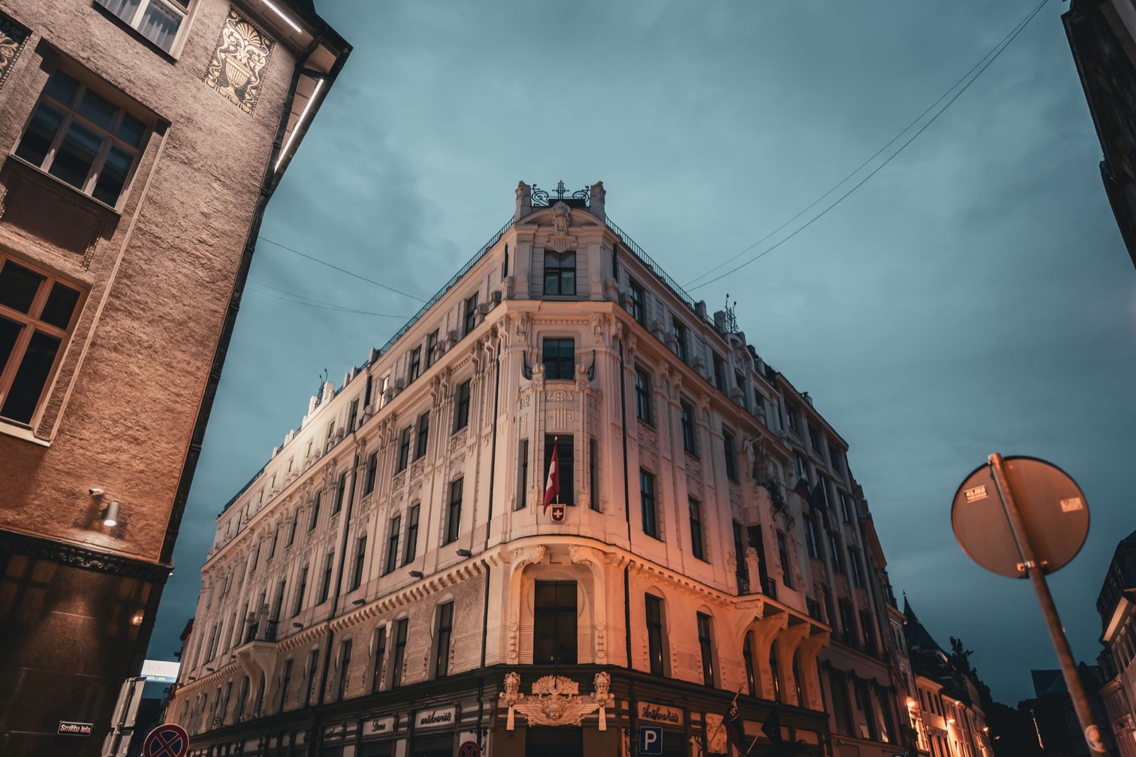 An ornate corner building lit against a dusk sky at the end of a narrow Riga street