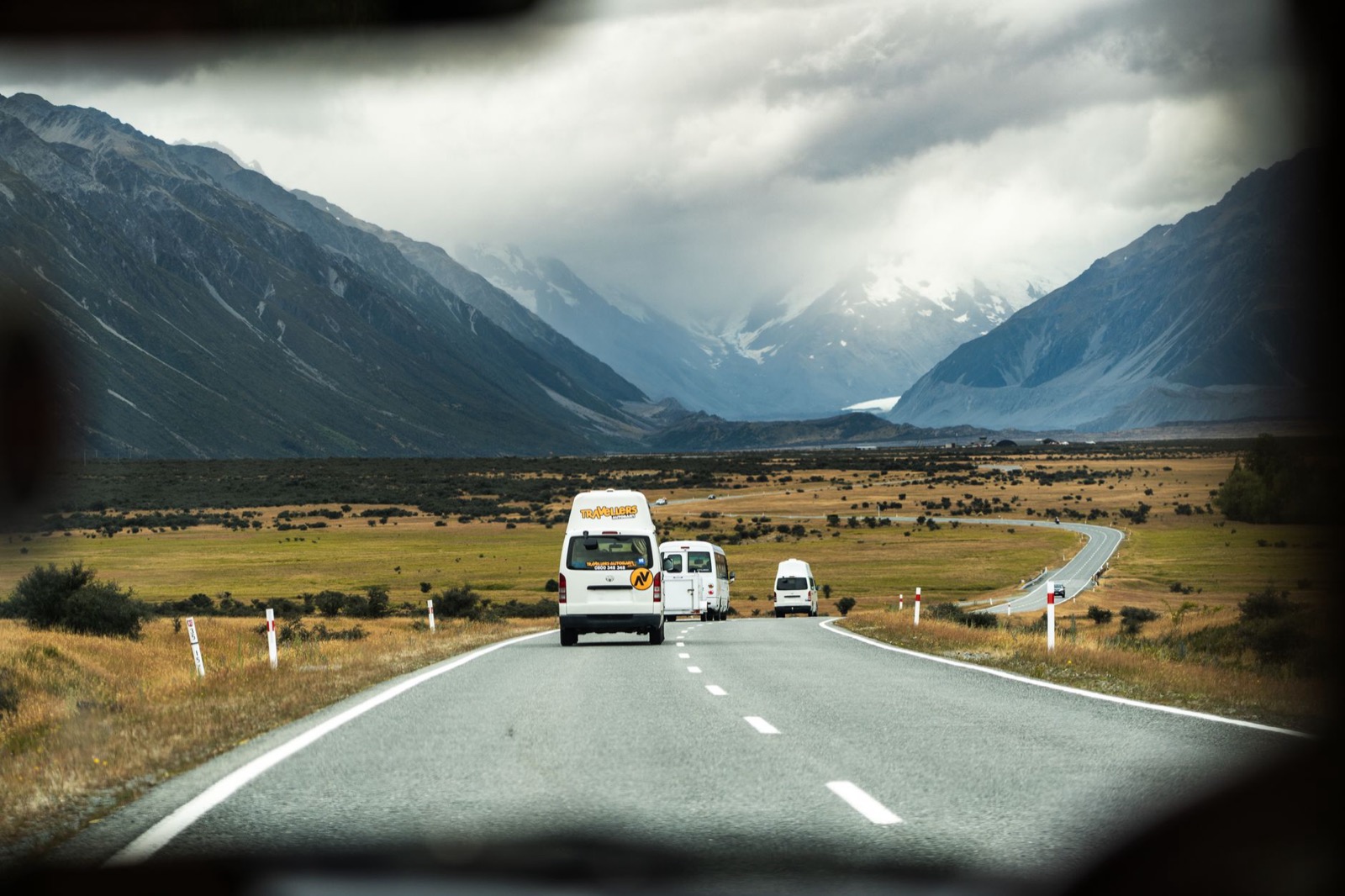 A white campervan parked on gravel beside a meadow below steep alpine slopes