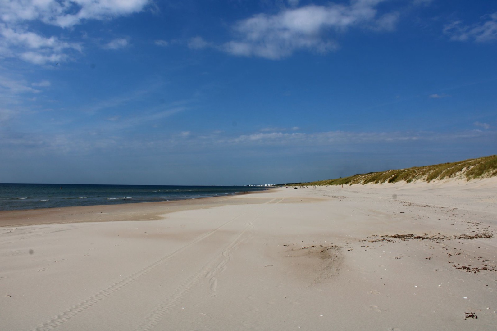 A wide empty sand beach running away to low grassy dunes under a blue sky