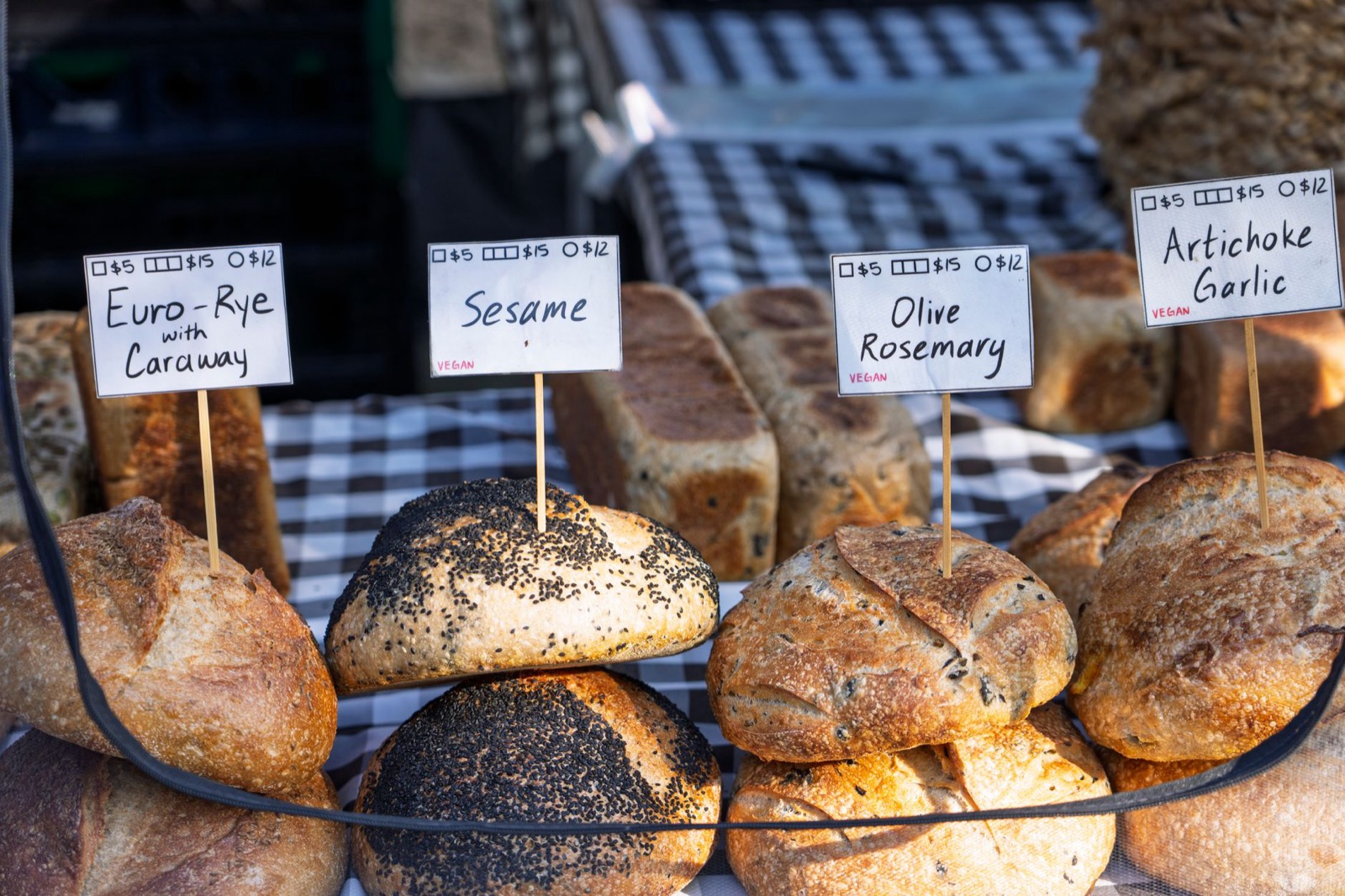 Round sourdough loaves on a market stall with handwritten variety cards