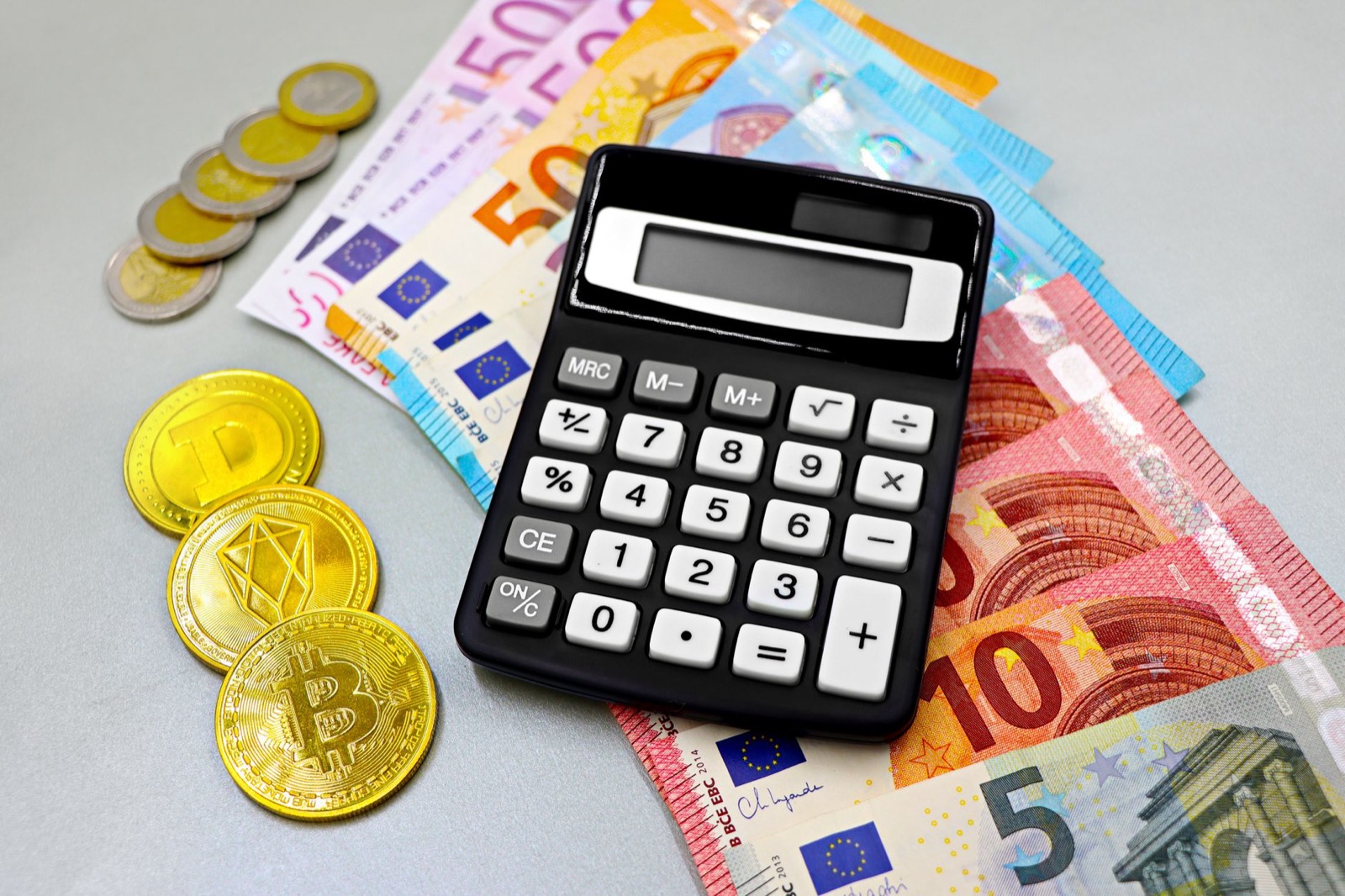 Euro banknotes, coins and novelty crypto tokens spread around a pocket calculator