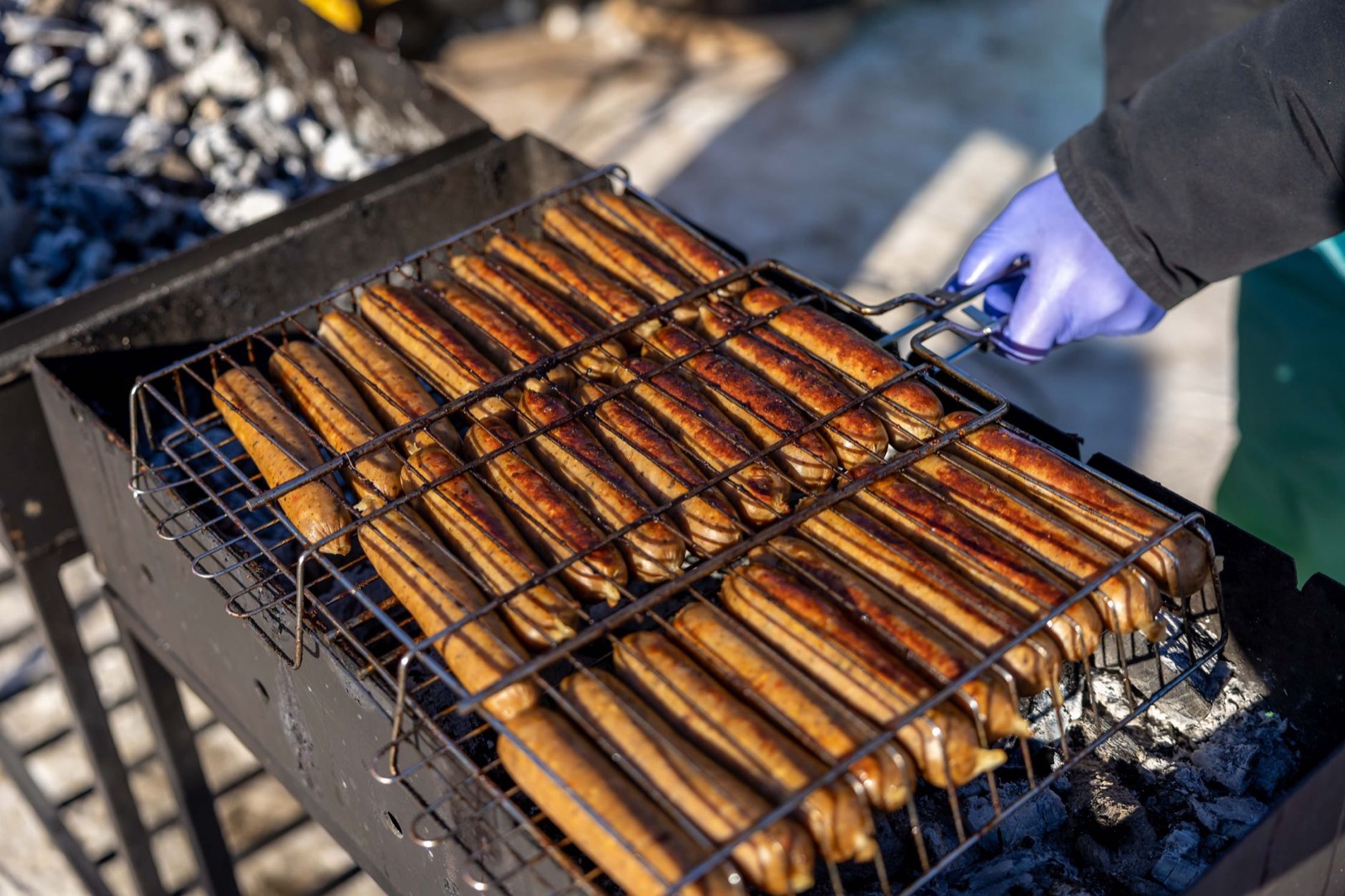Rows of long sausages browning under a wire rack on a charcoal grill