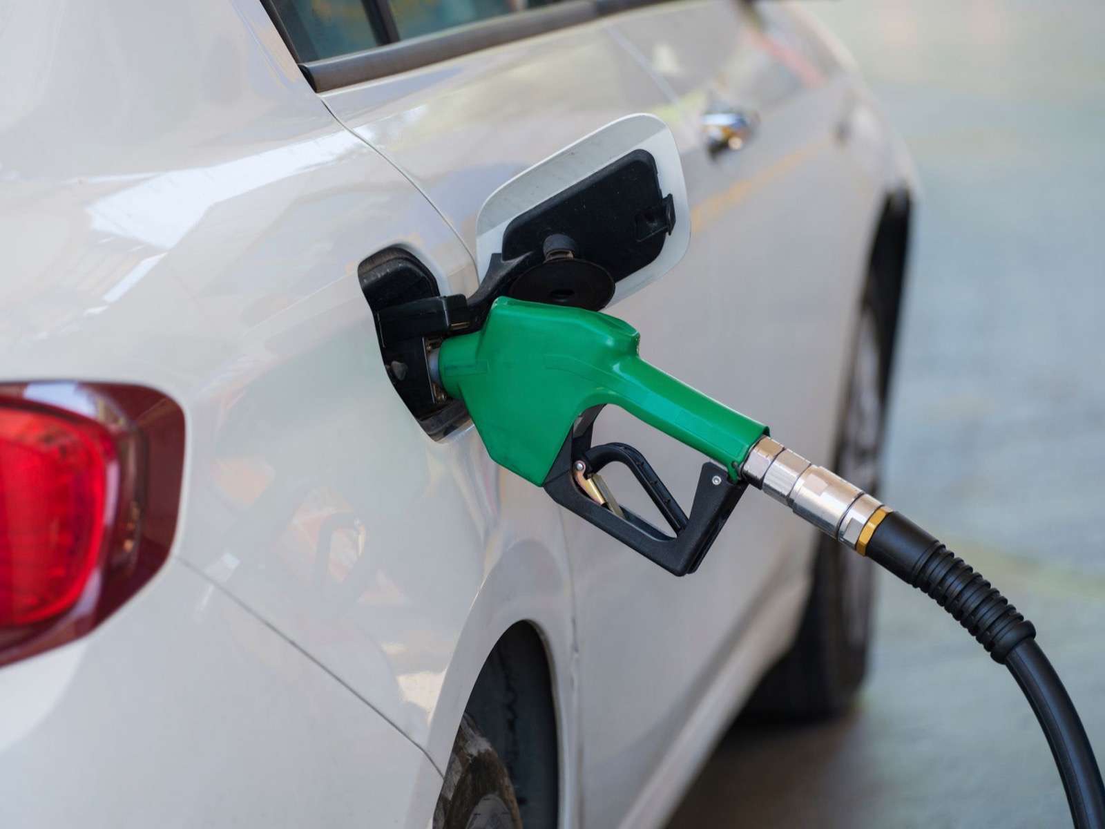 A green petrol nozzle in the filler of a white car at a pump