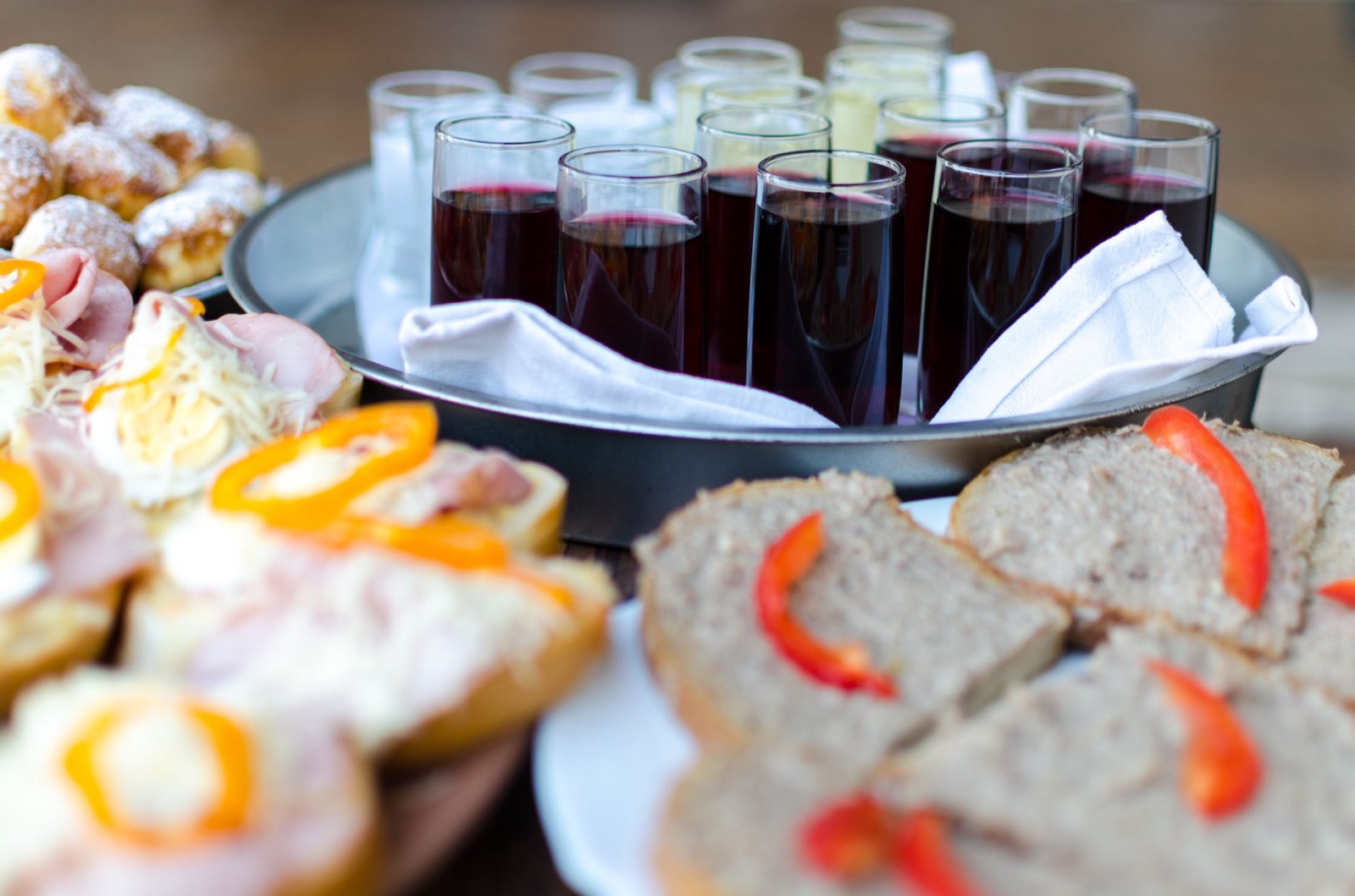 A tray of filled wine glasses behind platters of open sandwiches and pastries