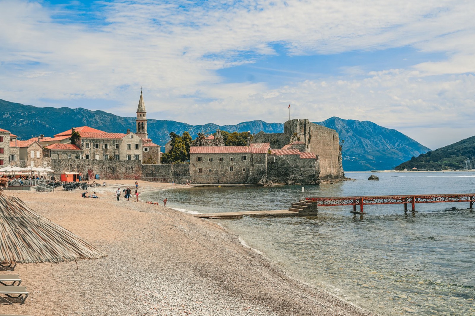 The walled old town and citadel of Budva above a sandy beach and a red pier