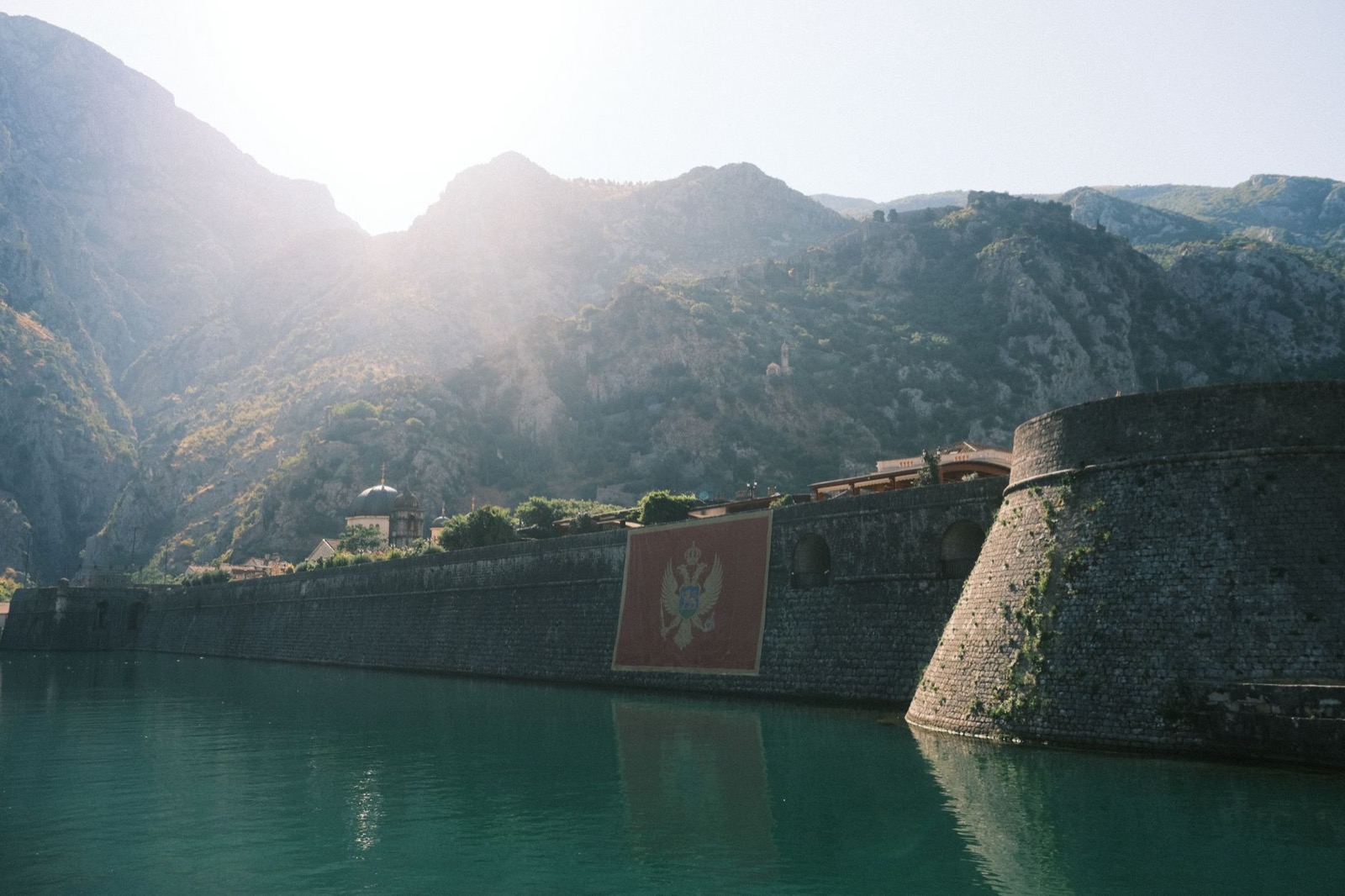 The stone sea wall of Kotor hung with a Montenegrin flag below steep grey mountains