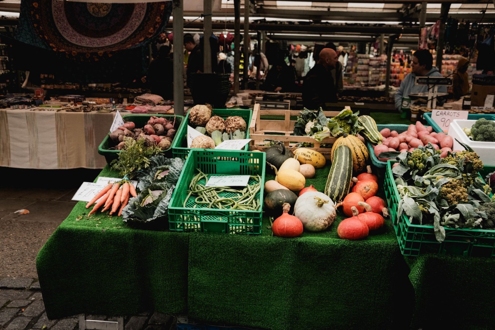 An open-air stall with crates of squash, broccoli, carrots and beans laid out on a green cloth