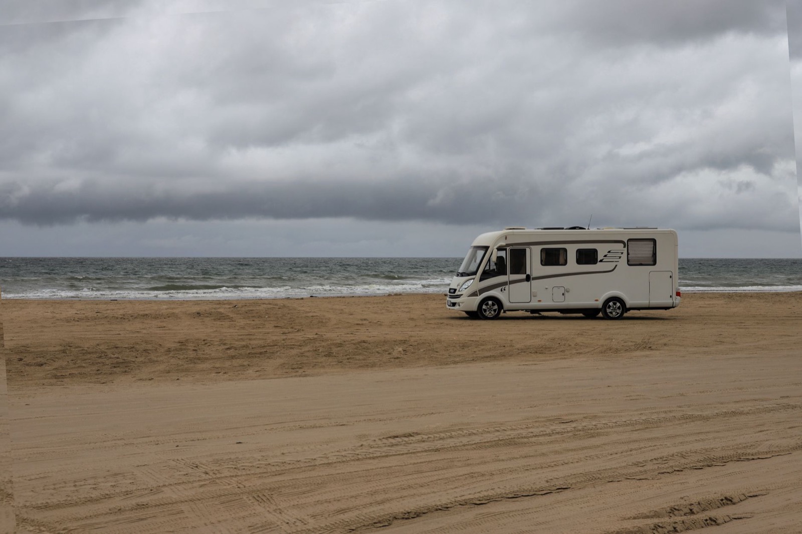 A large motorhome standing on a wide flat beach under heavy grey cloud, the North Sea behind it