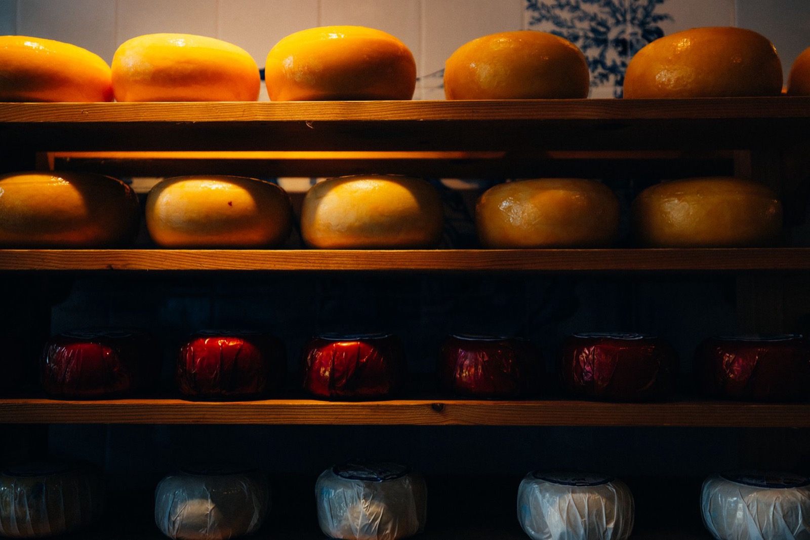 Rows of gouda wheels on wooden shelves above red waxed cheeses