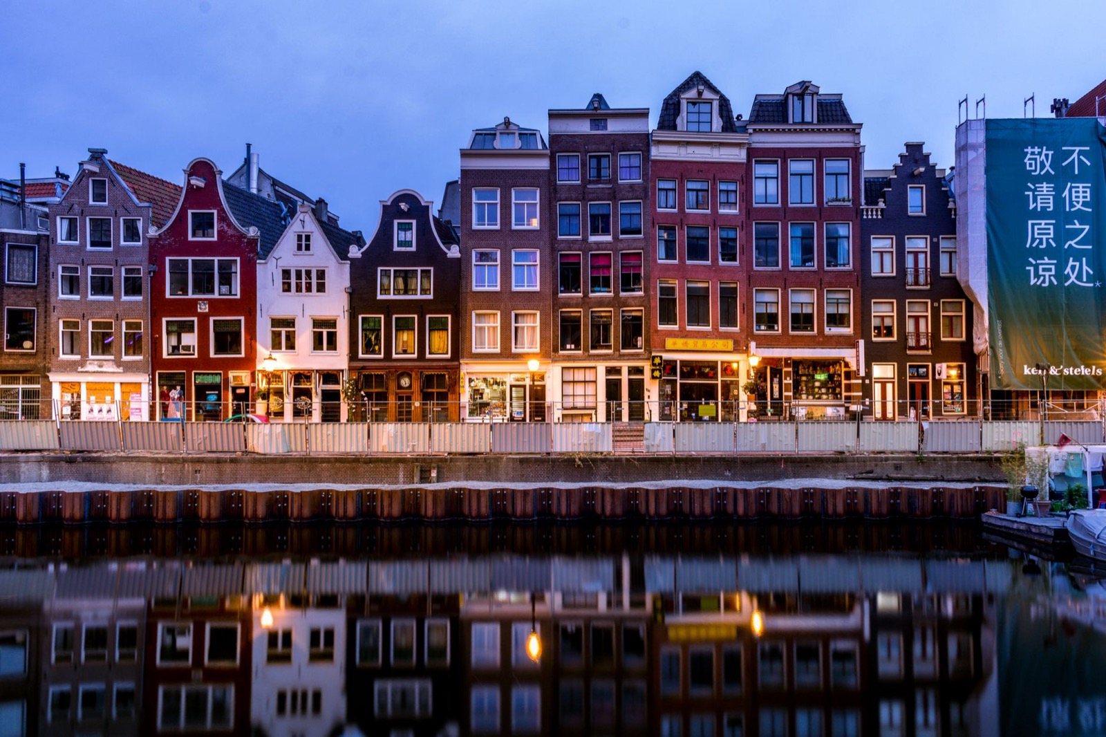 Tall gabled canal houses reflected in still water in a Dutch city at dusk
