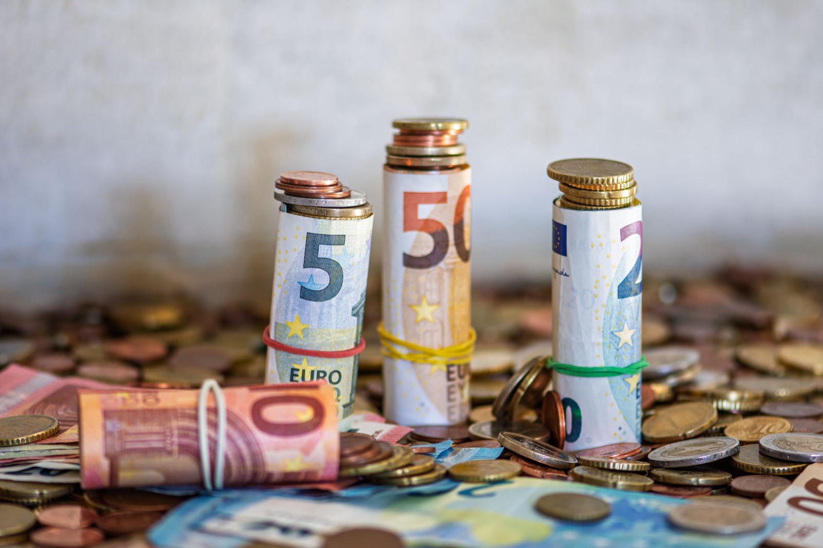 Rolled euro banknotes standing on a heap of loose euro coins and notes