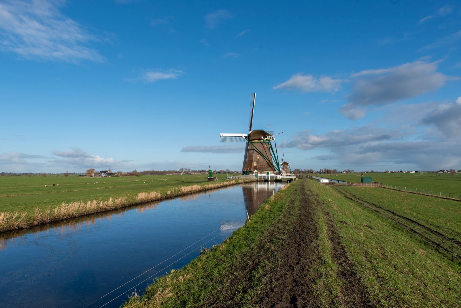 A windmill beside a straight canal in flat Dutch polder land under tall clouds