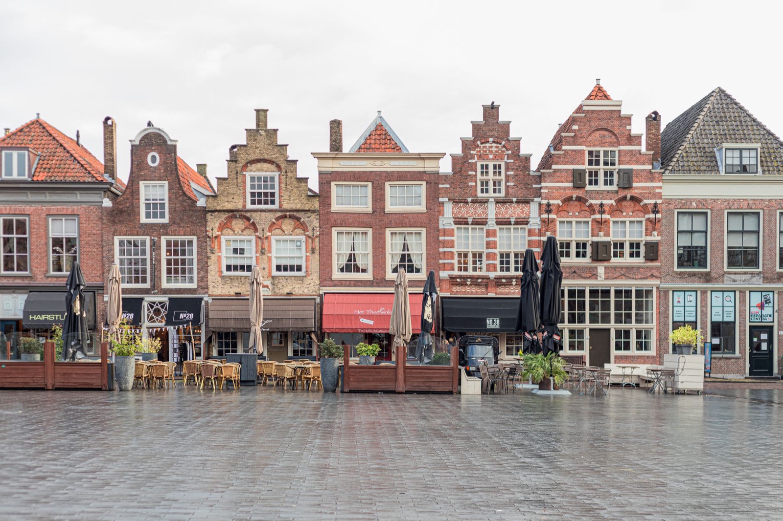 Dutch stepped gable houses along a wet empty market square with closed cafe terraces