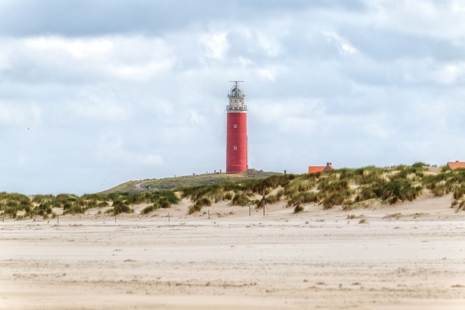 A lighthouse above dunes and a wide empty beach on a Wadden island