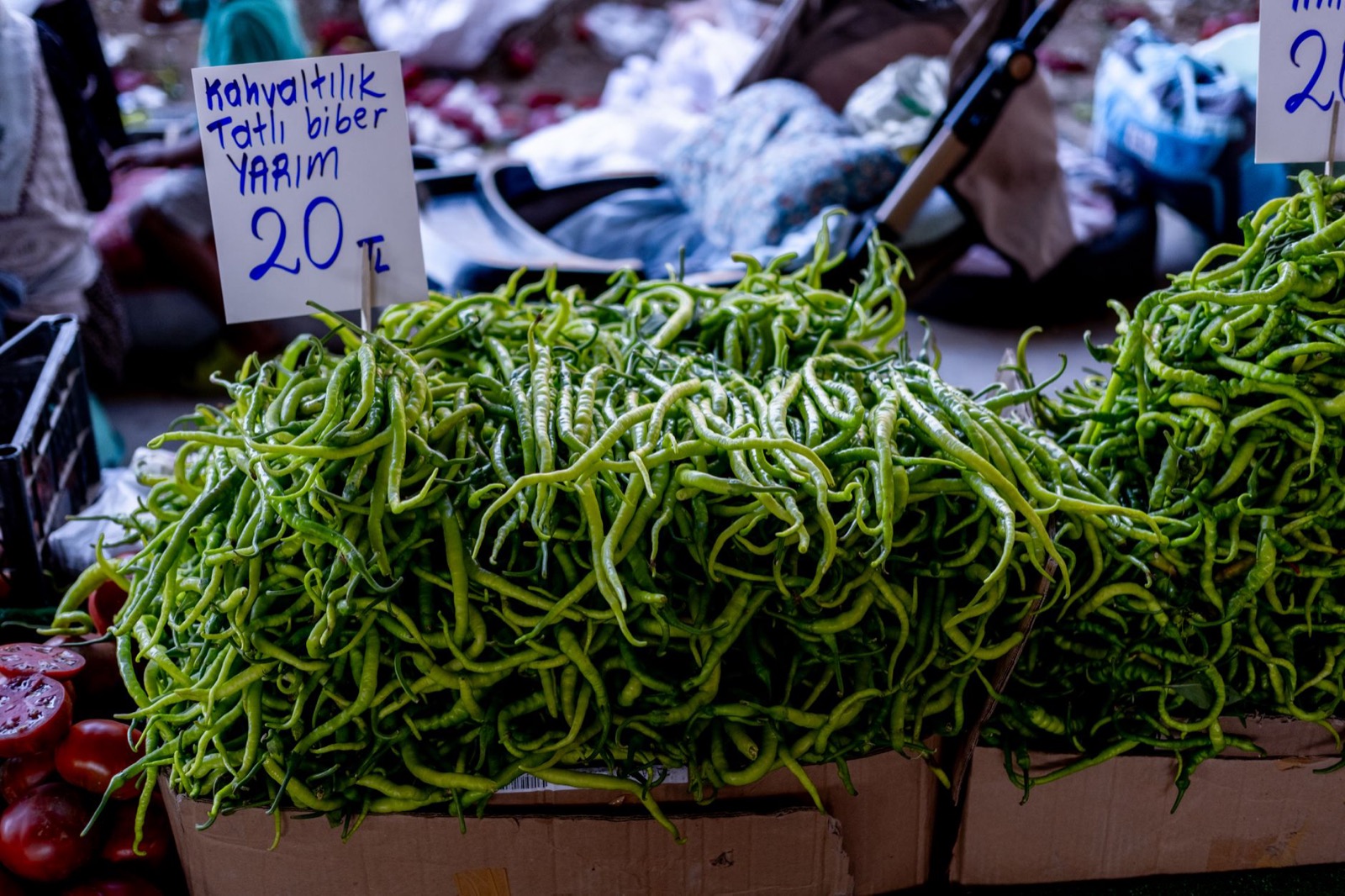 Crates of long green peppers on a market stall behind a handwritten price sign