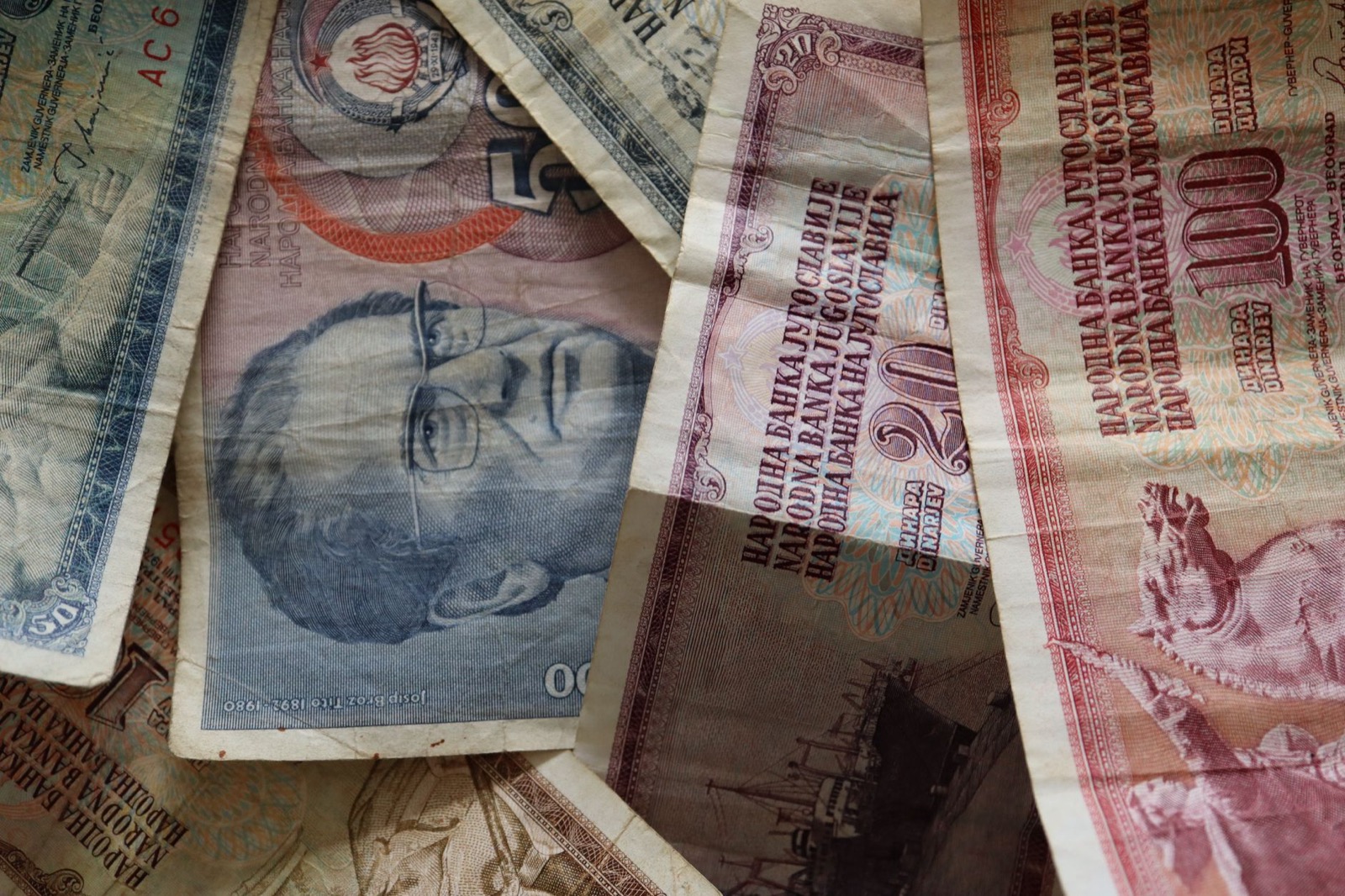 Worn Yugoslav dinar banknotes overlapping, one of them carrying a portrait of Tito