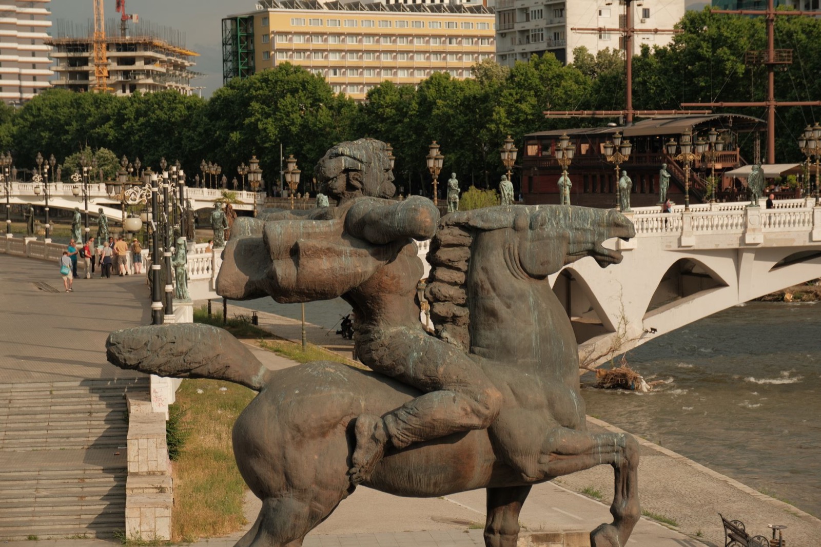 Bronze horse statues on the Vardar embankment in Skopje beside a white balustraded bridge lined with sculptures