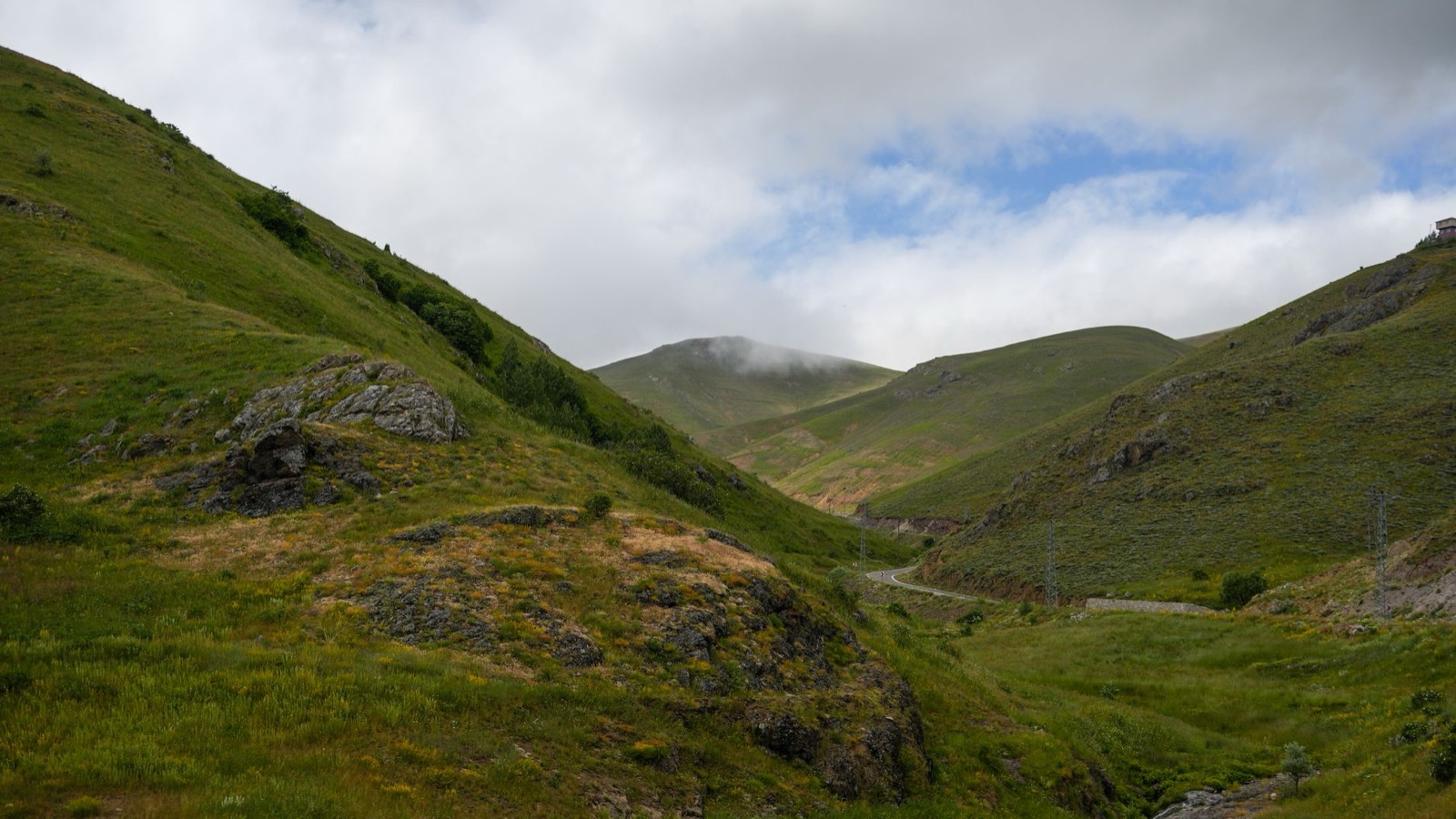 A road threading a green valley between rounded hills under low cloud