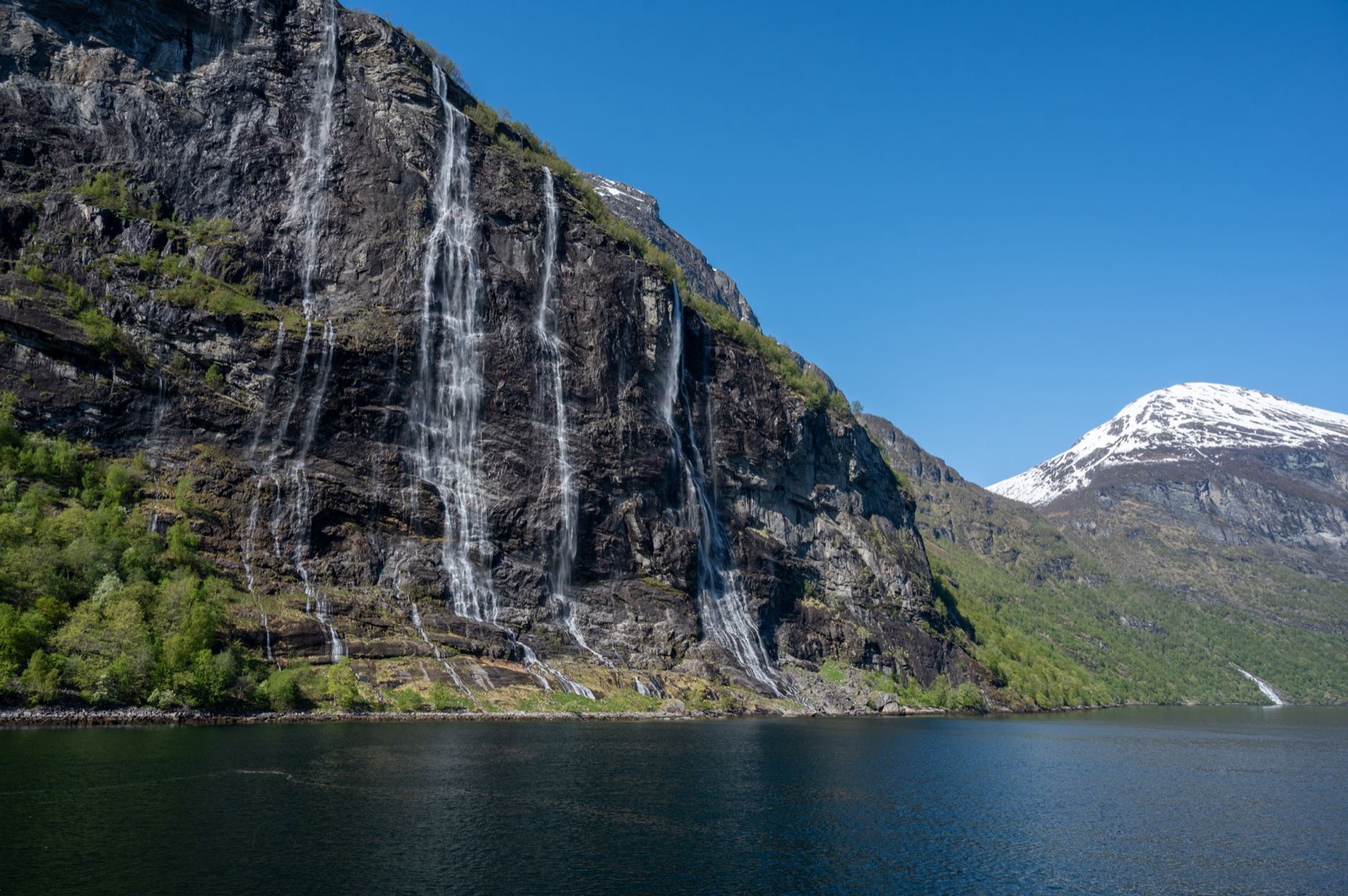 A deep fjord with waterfalls falling from green cliffs into dark water