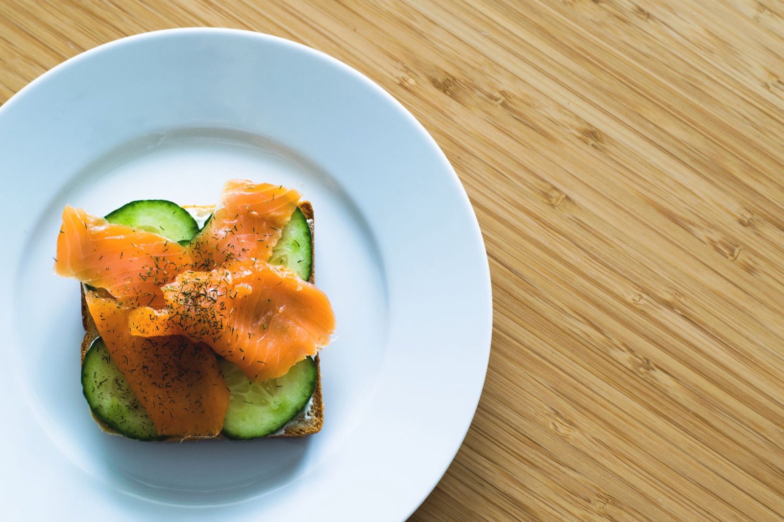 An open sandwich of smoked salmon, cucumber and dill on a white plate