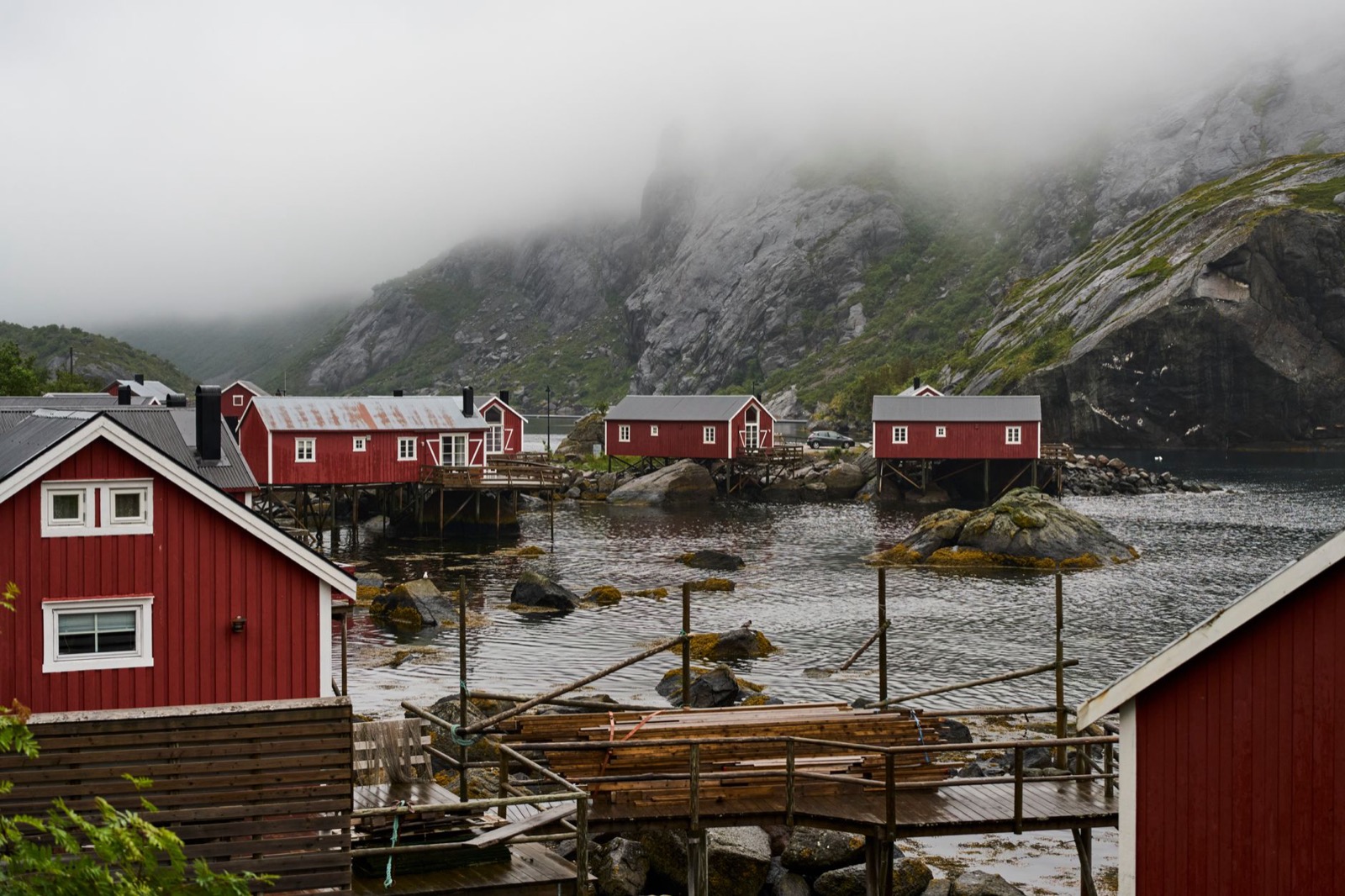 Red fishermen's cabins on stilts below mist-covered granite peaks in Lofoten