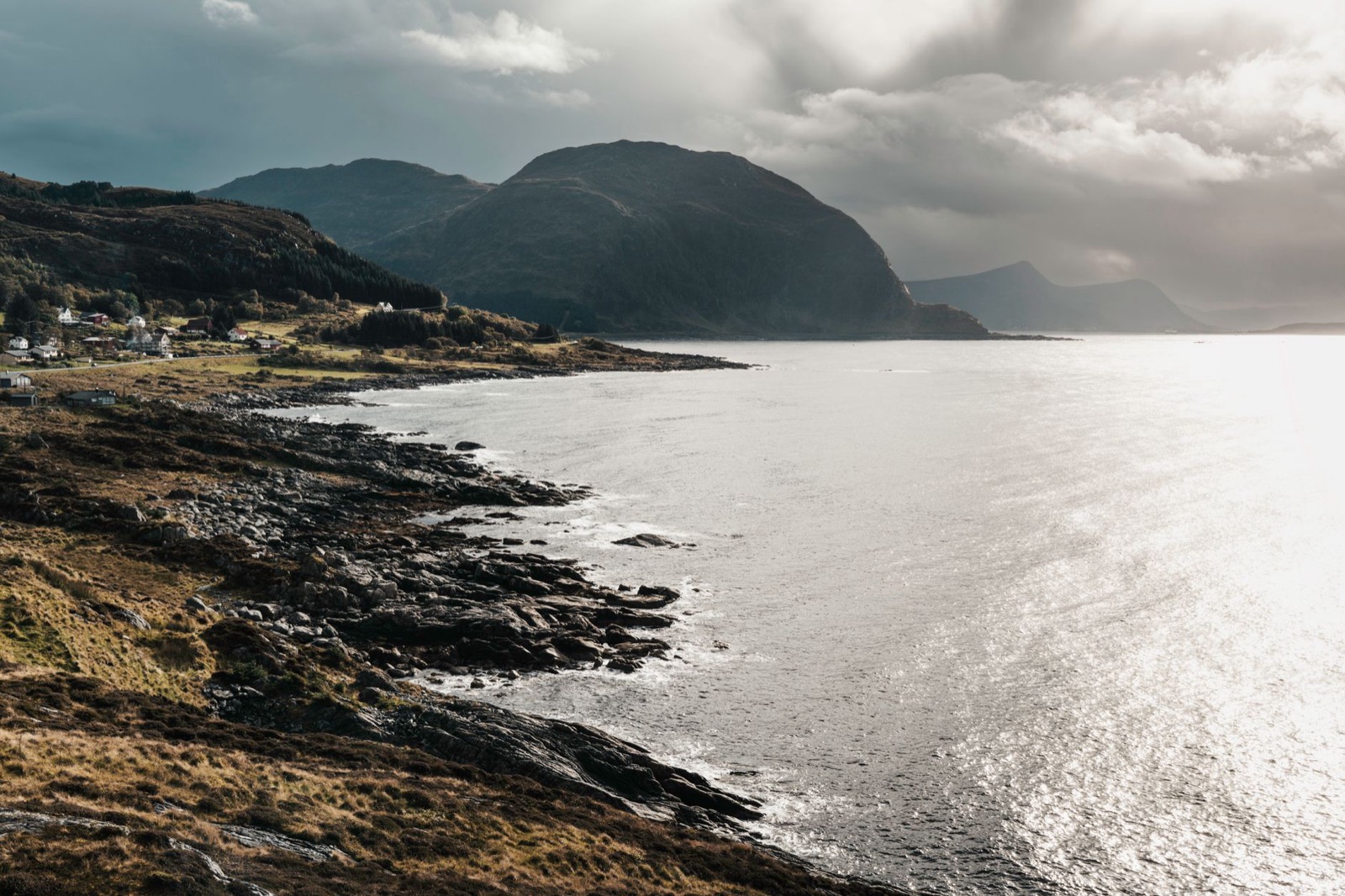 A low sun over the sea behind a rocky coastline with a few houses on the shore