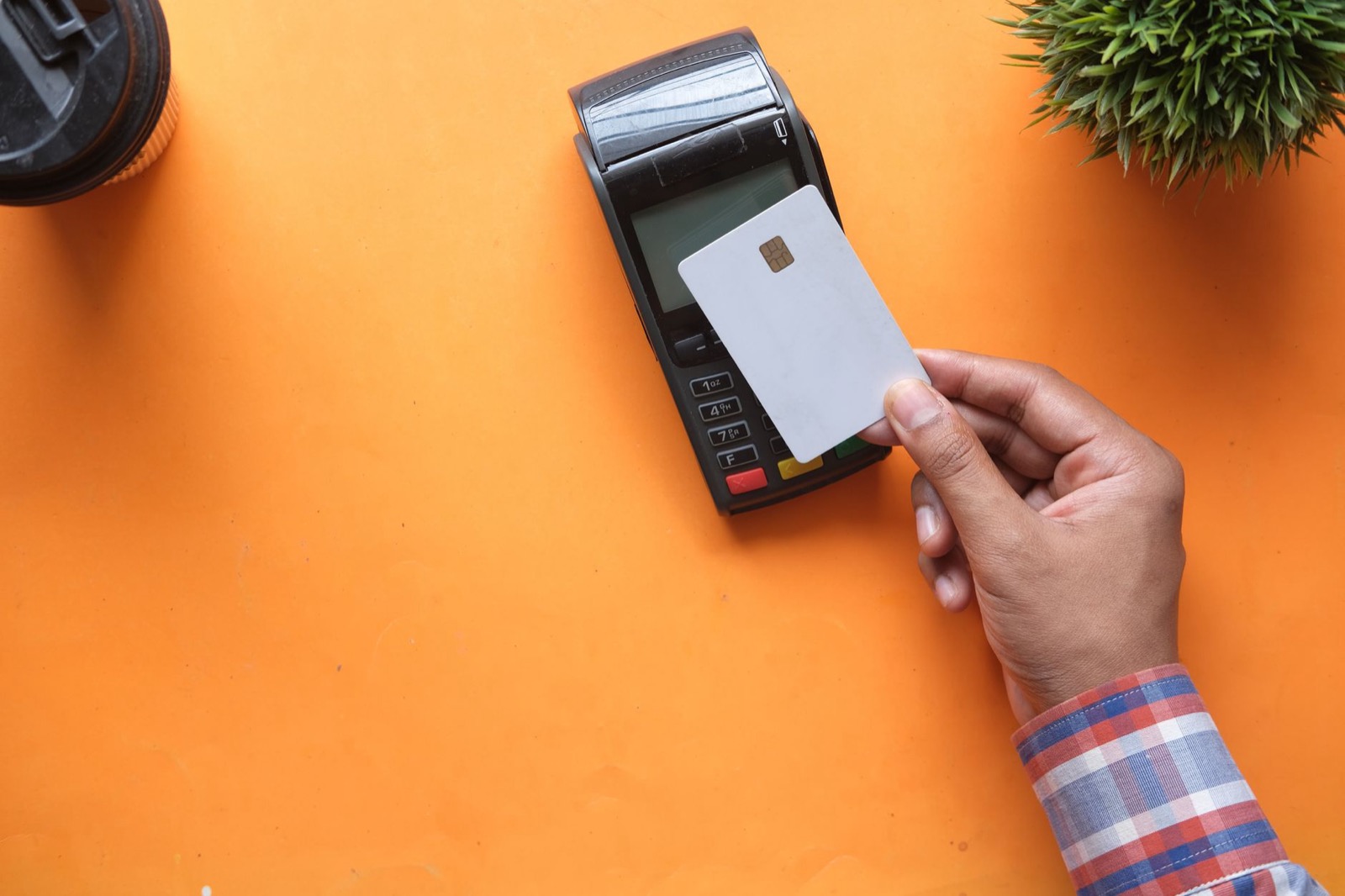 A hand holding a bank card against a card terminal on an orange desk