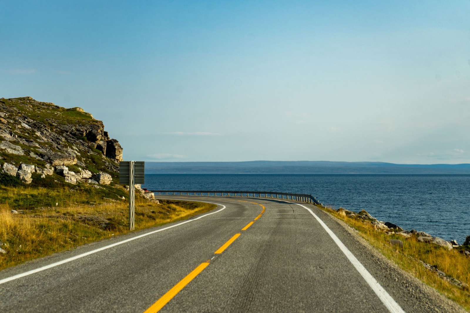 An empty road curving along a bare rocky coast above the sea