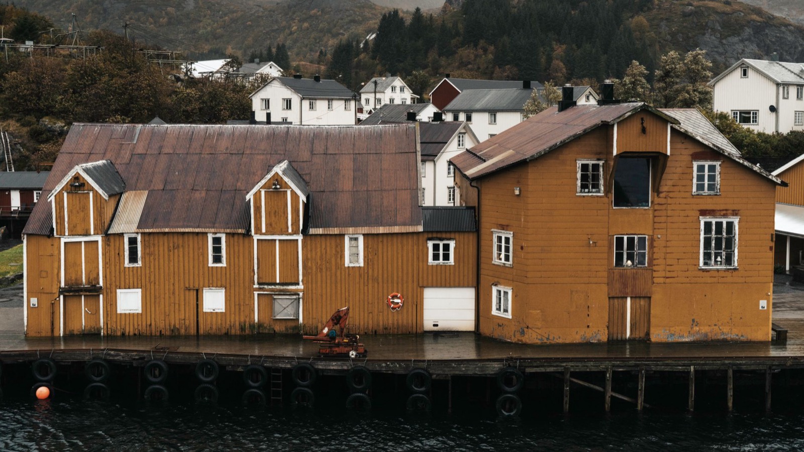 Ochre-painted wooden warehouses along a quayside, with white houses on the hillside behind