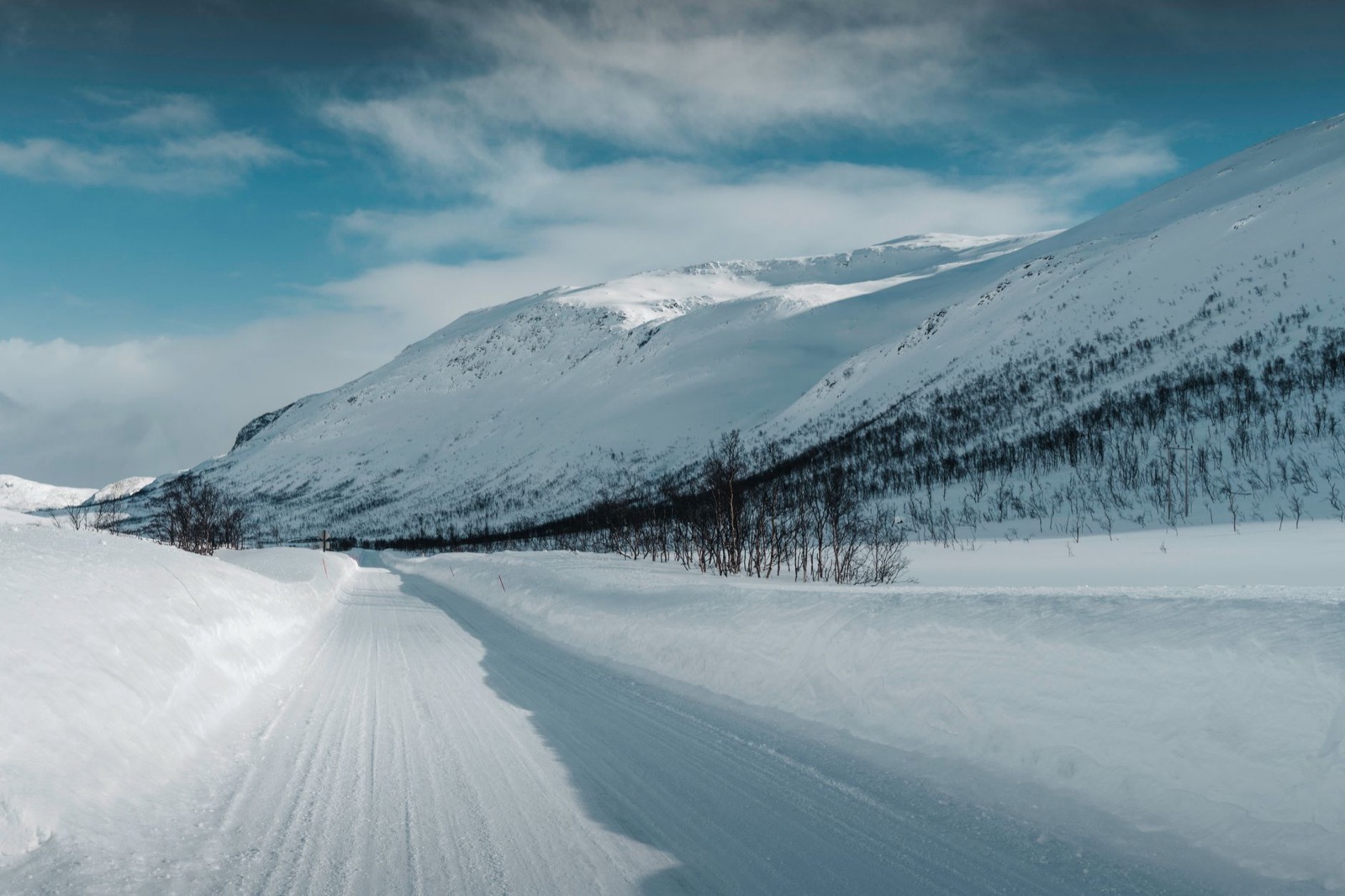 A snow-covered mountain road between deep snowbanks under a bright winter sky