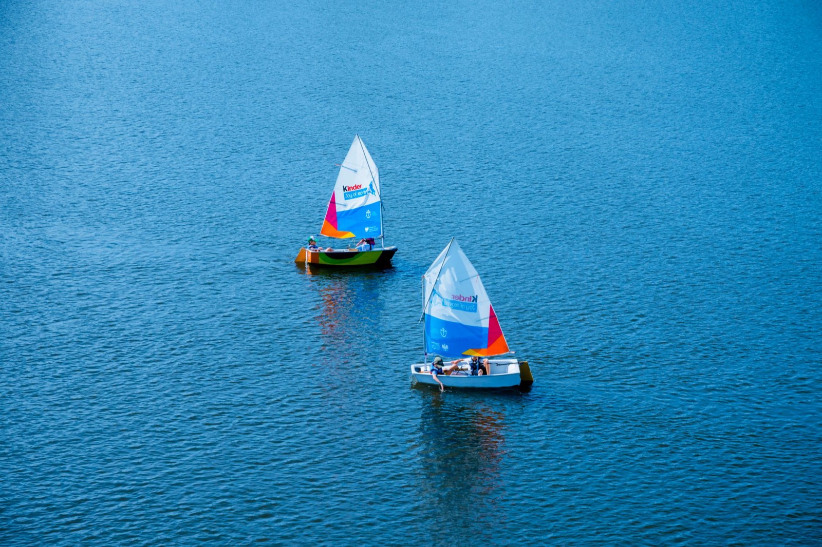 Two small sailing dinghies with coloured sails on open blue lake water