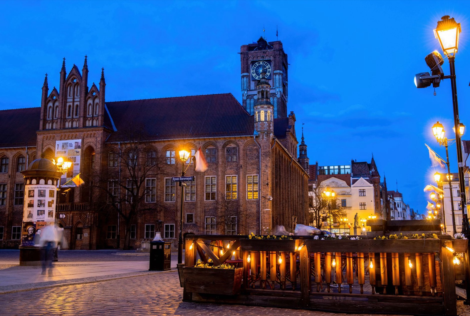 A Gothic town hall and lit street lamps on a Polish market square at blue hour