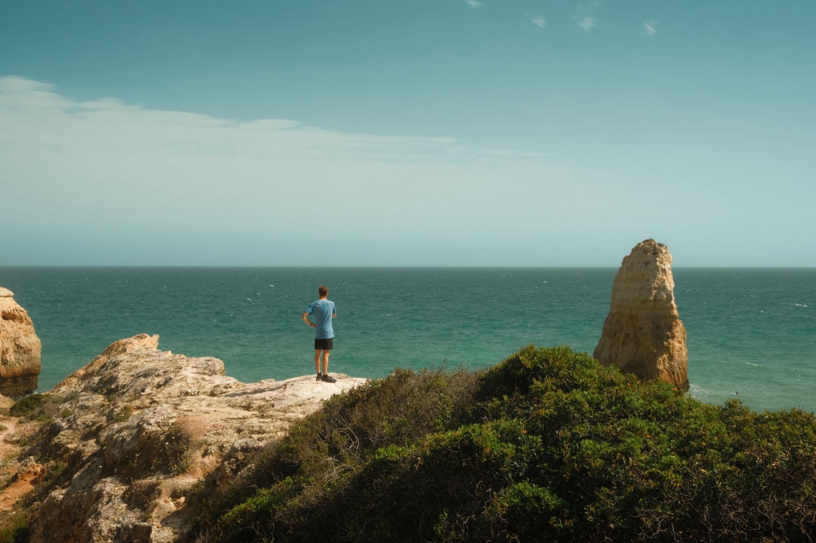 A traveller standing above the Atlantic beside a tall sandstone sea stack