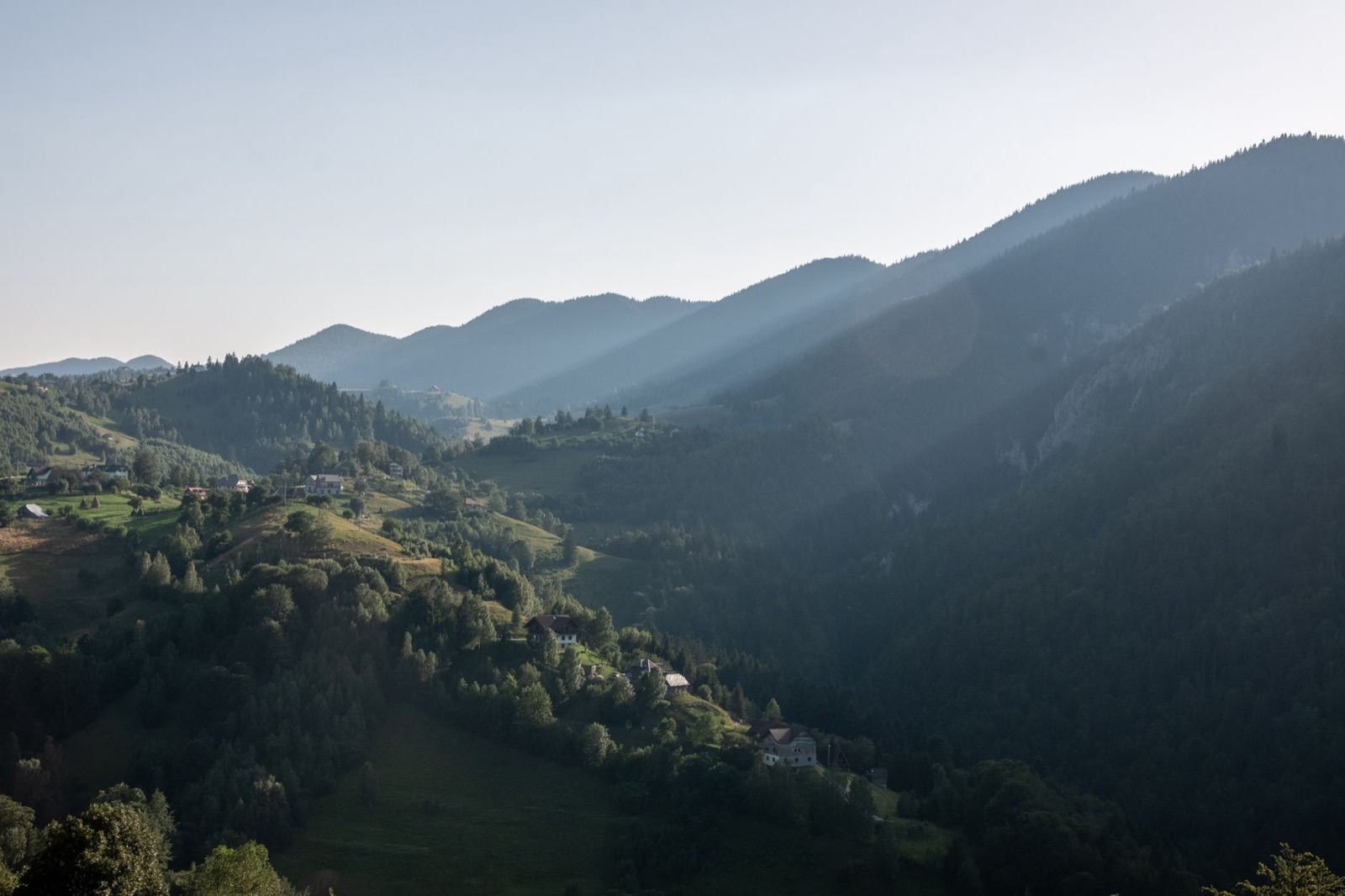 Scattered farmsteads on wooded slopes with hazy ridges receding behind them