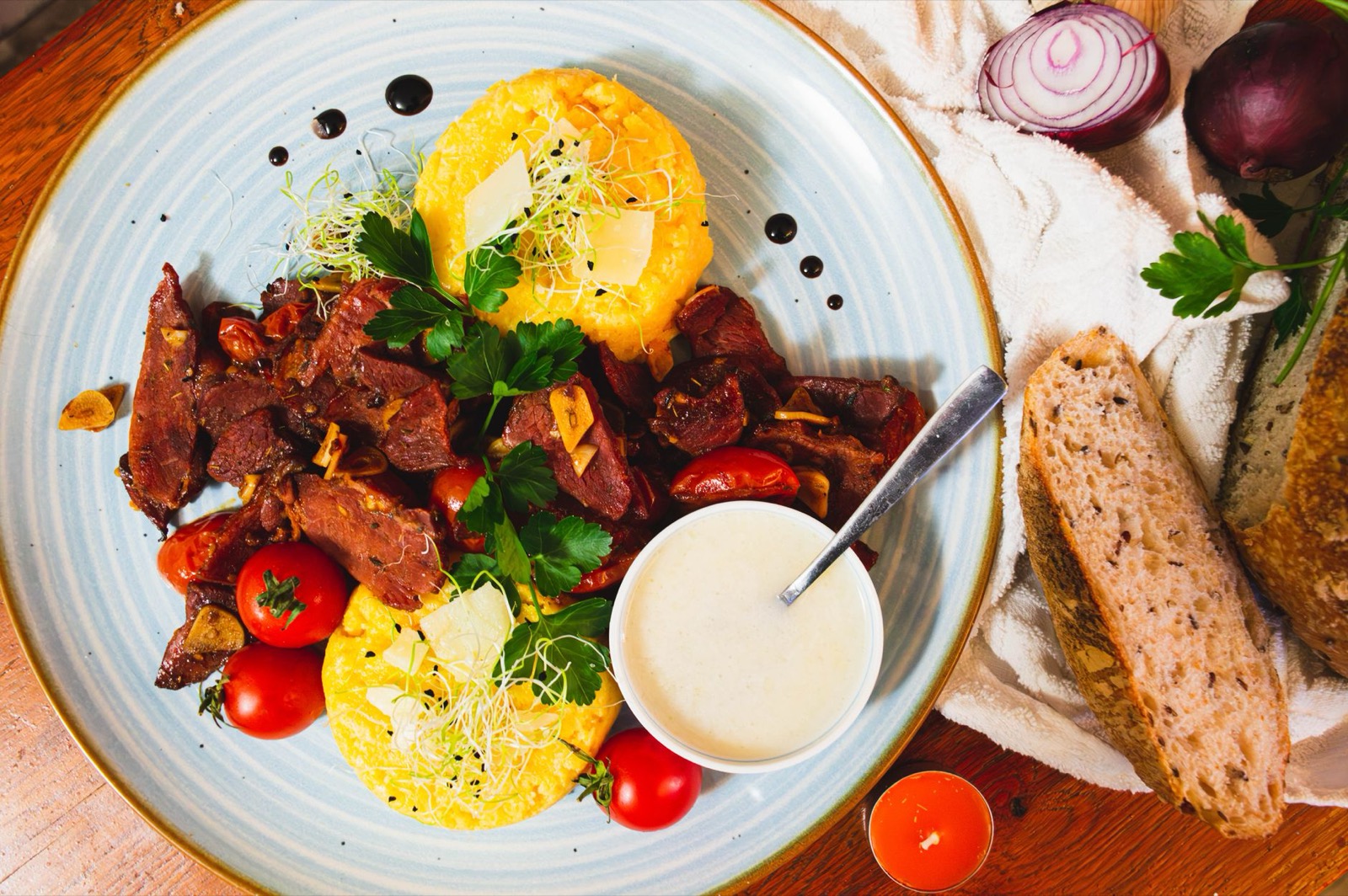 Rounds of polenta with sautéed meat, cherry tomatoes and a small bowl of sour cream