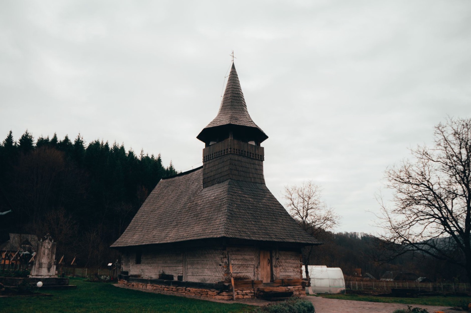 A tall shingled wooden church with a narrow spire in a Maramures village