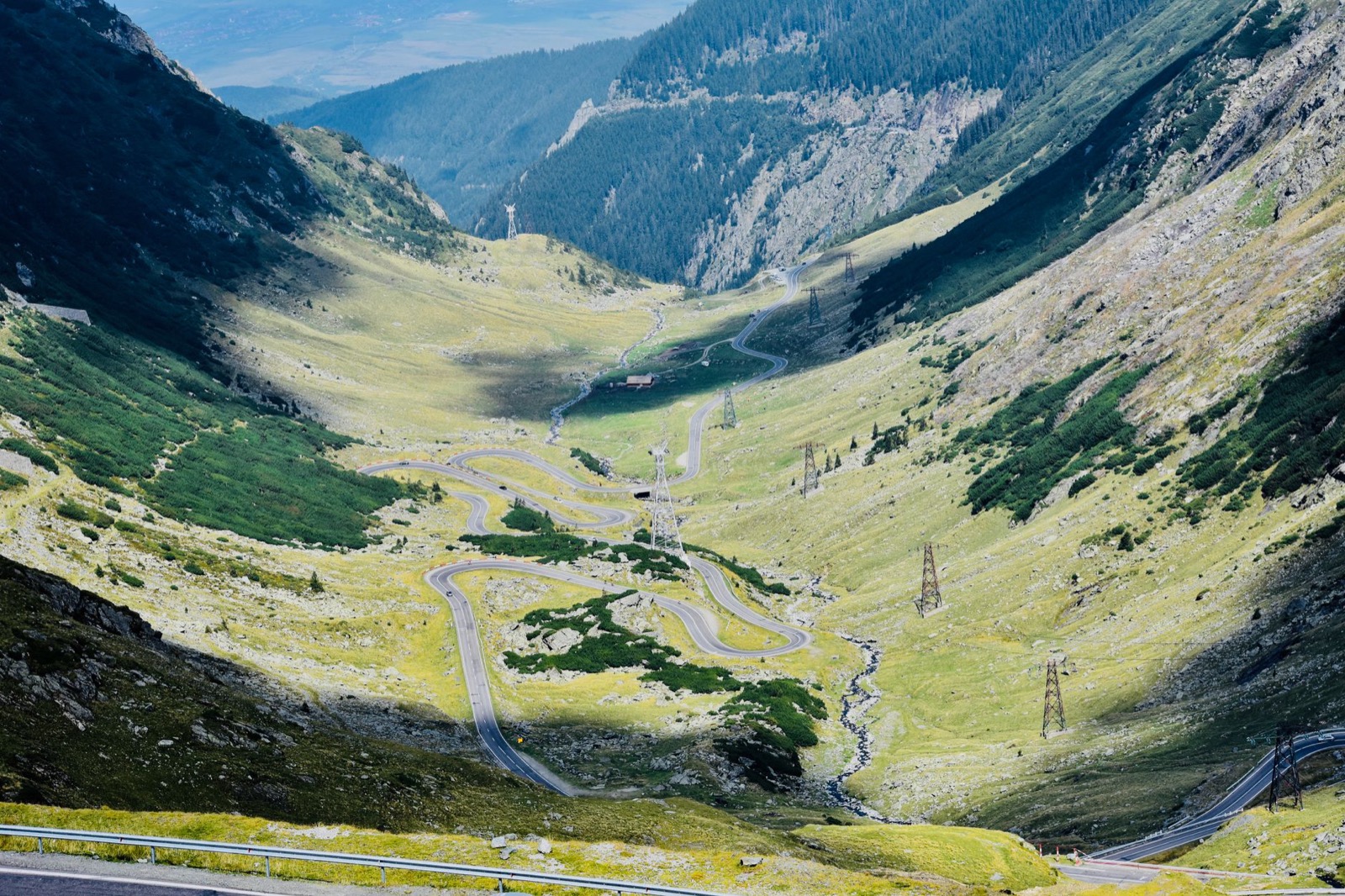 Hairpin bends of the Transfagarasan road stacked up a green glacial valley below rock walls