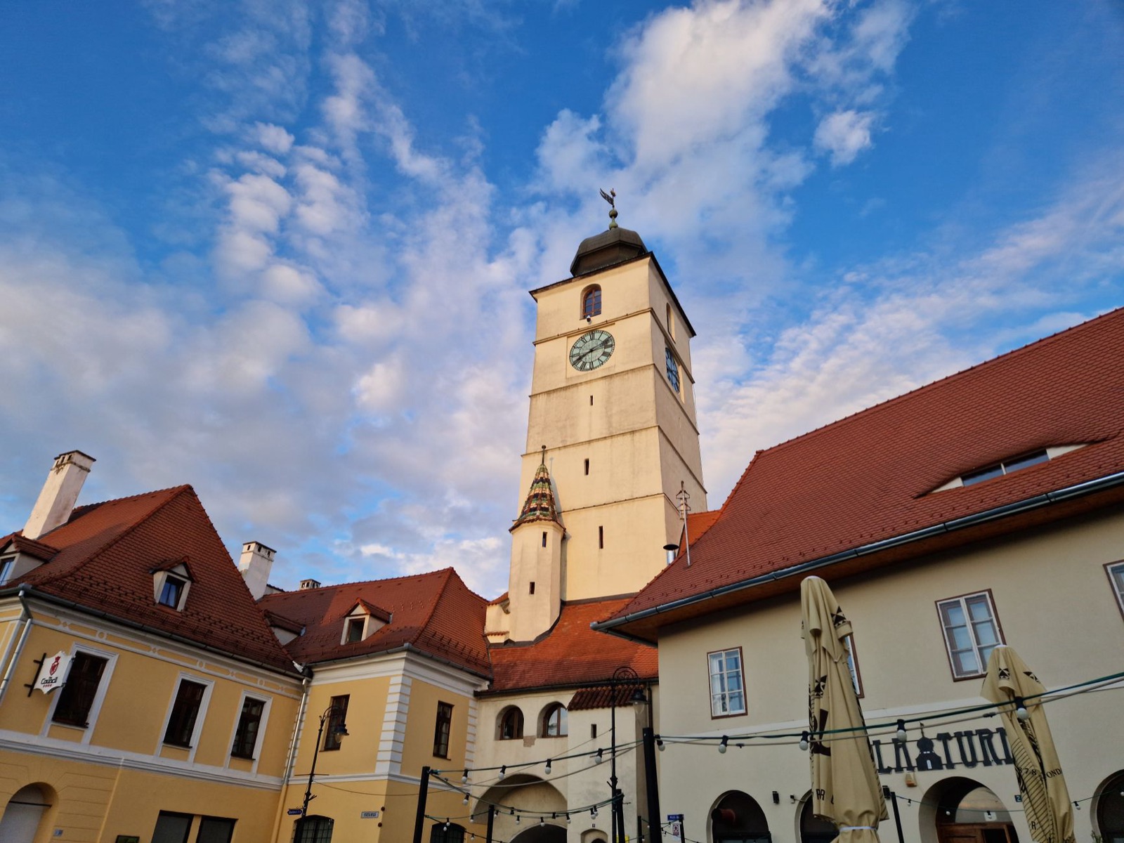 A clock tower rising above red-tiled roofs and pale painted houses on an old town square