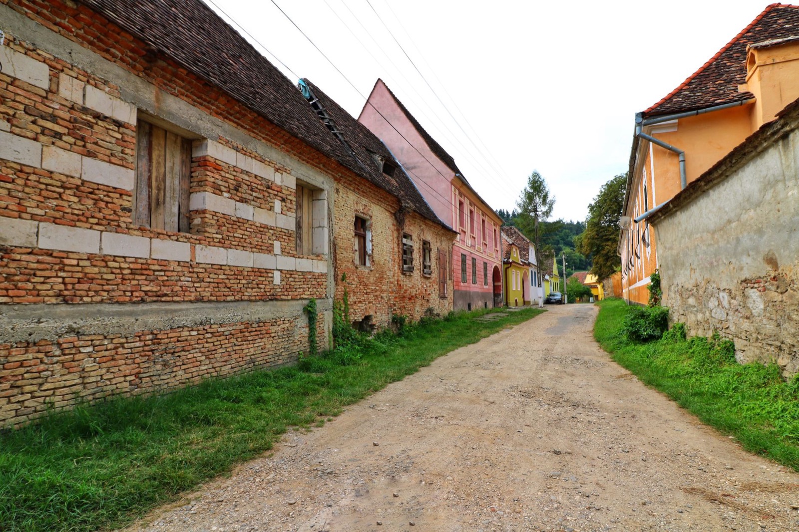 An unpaved village street between old brick and rendered houses painted pink and ochre
