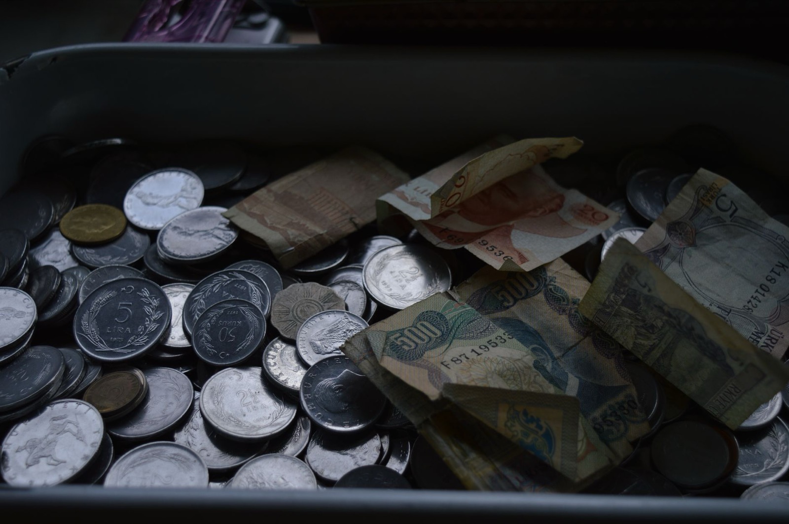 A tray of worn banknotes and a heap of mixed coins in low light