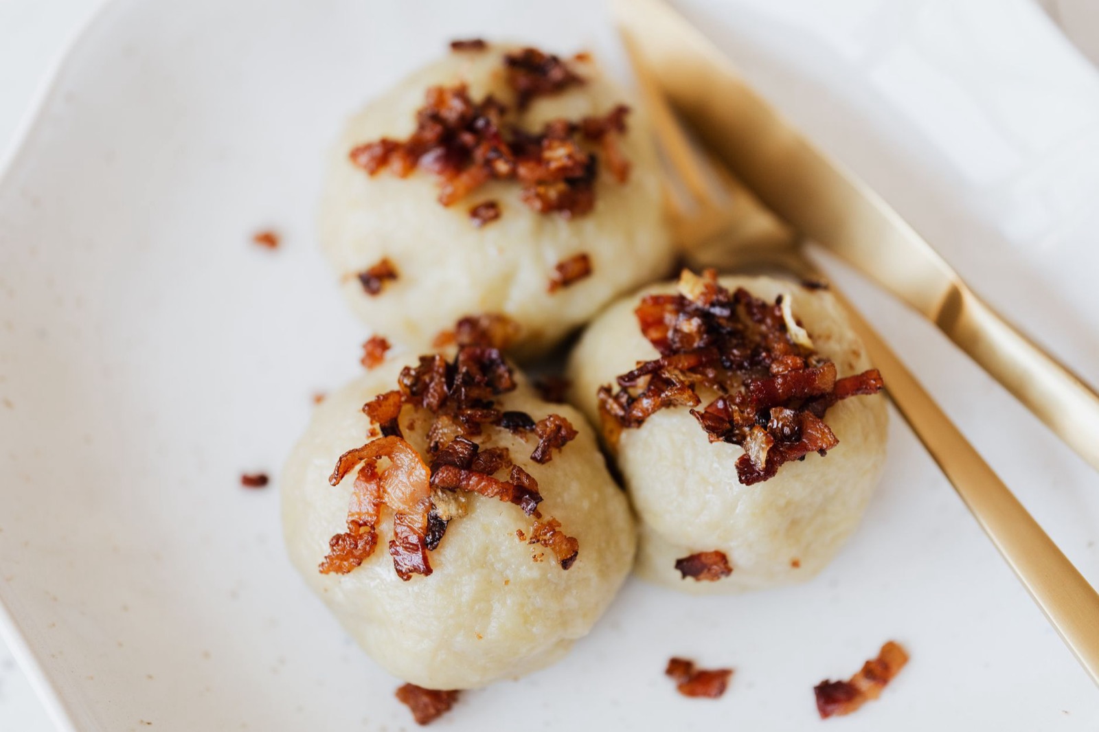 Three potato dumplings topped with crisp fried bacon on a white plate