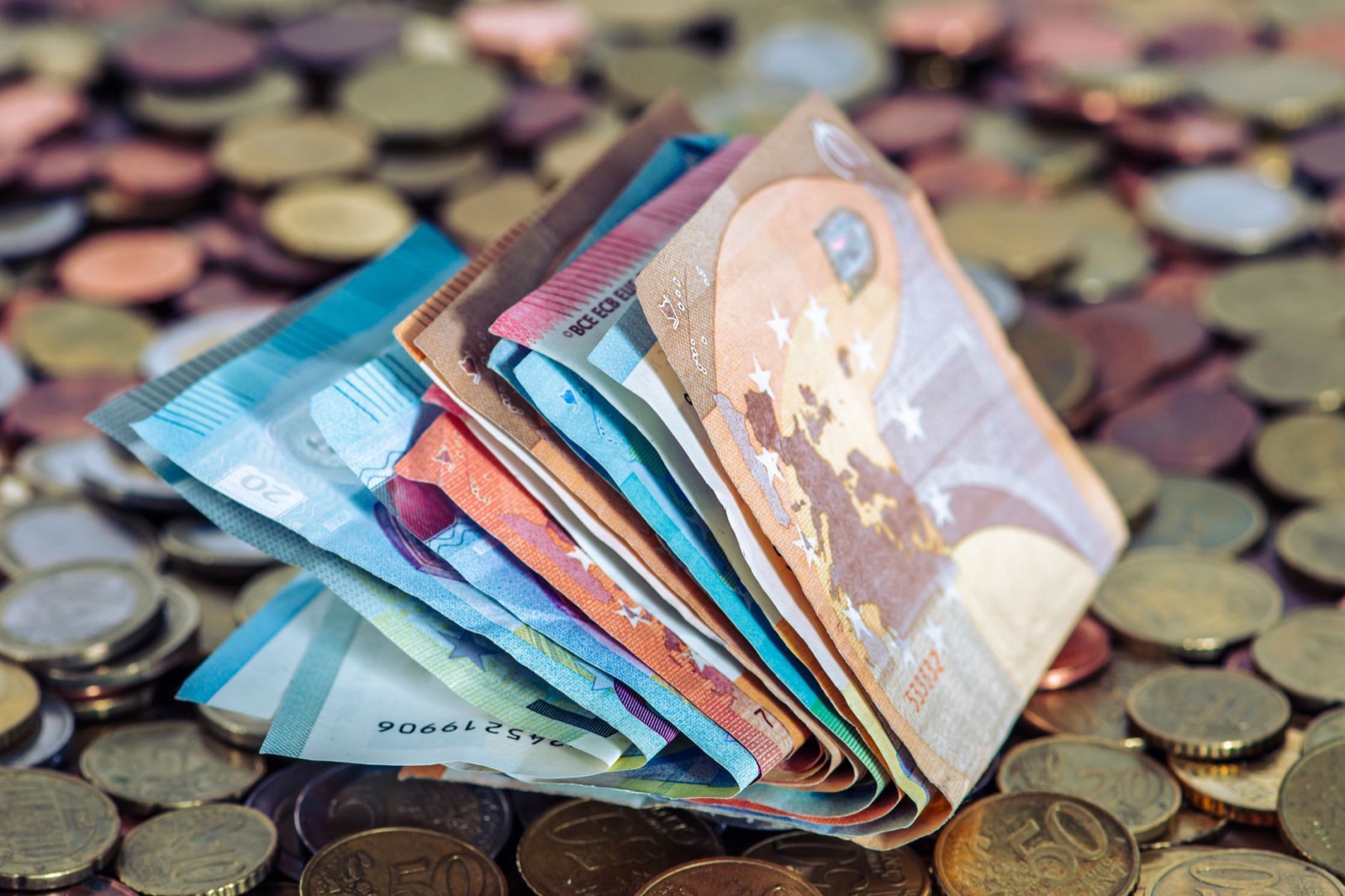 A fan of euro banknotes standing upright on a scattered bed of euro coins