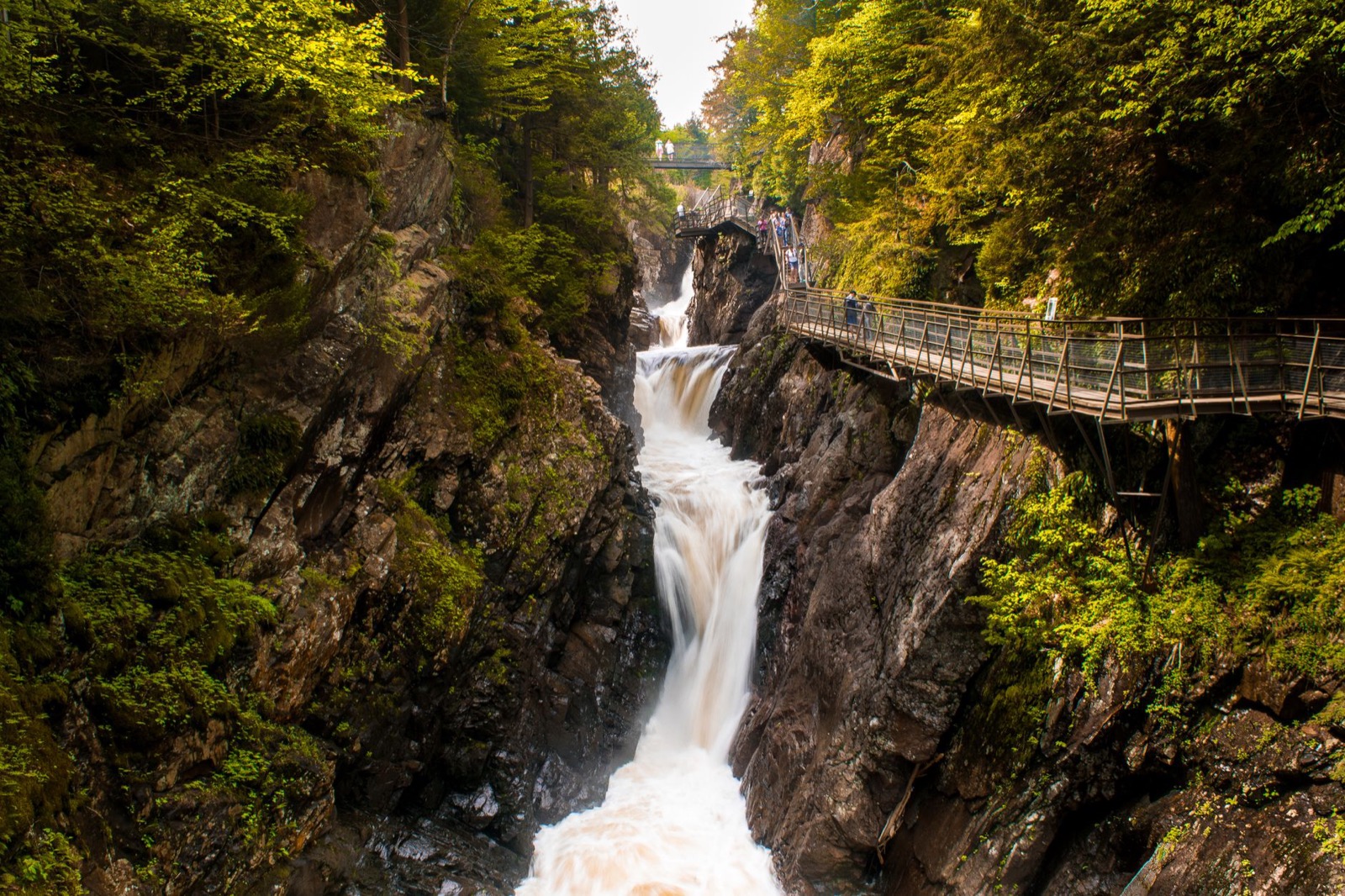 A waterfall dropping through a narrow rocky gorge with a walkway bolted to the cliff beside it