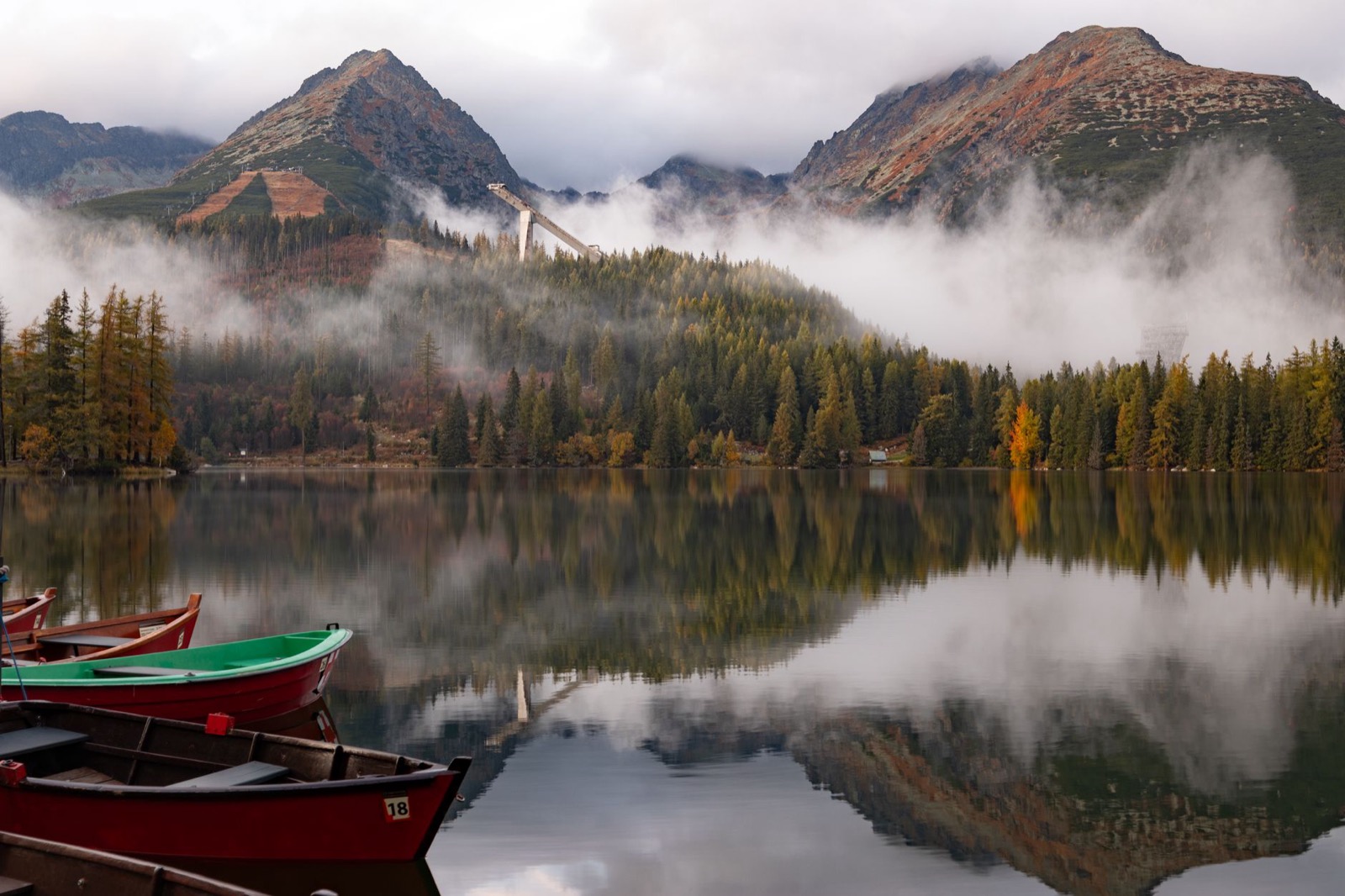 Rowing boats drawn up on a still mountain lake with mist lifting off larch forest and peaks behind