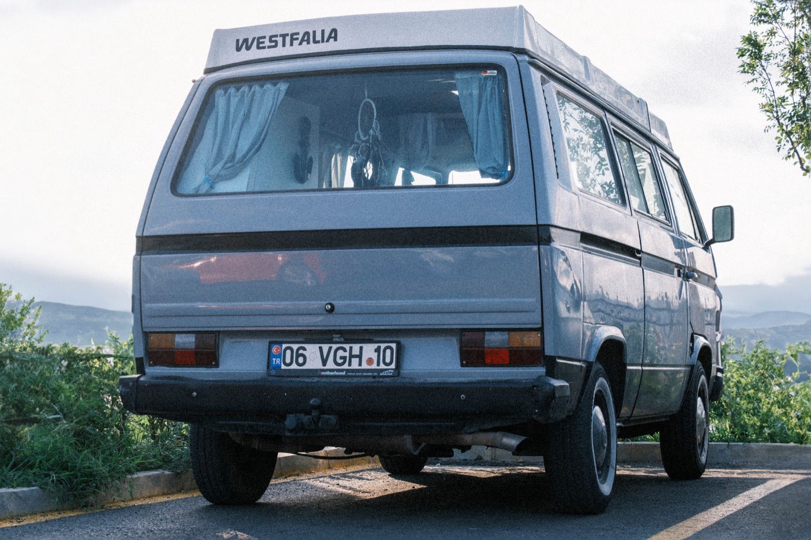 The rear of a grey pop-top campervan parked on the edge of a road above a hazy valley