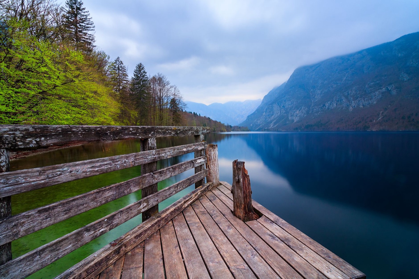 A weathered wooden jetty on a still alpine lake below steep forested mountains