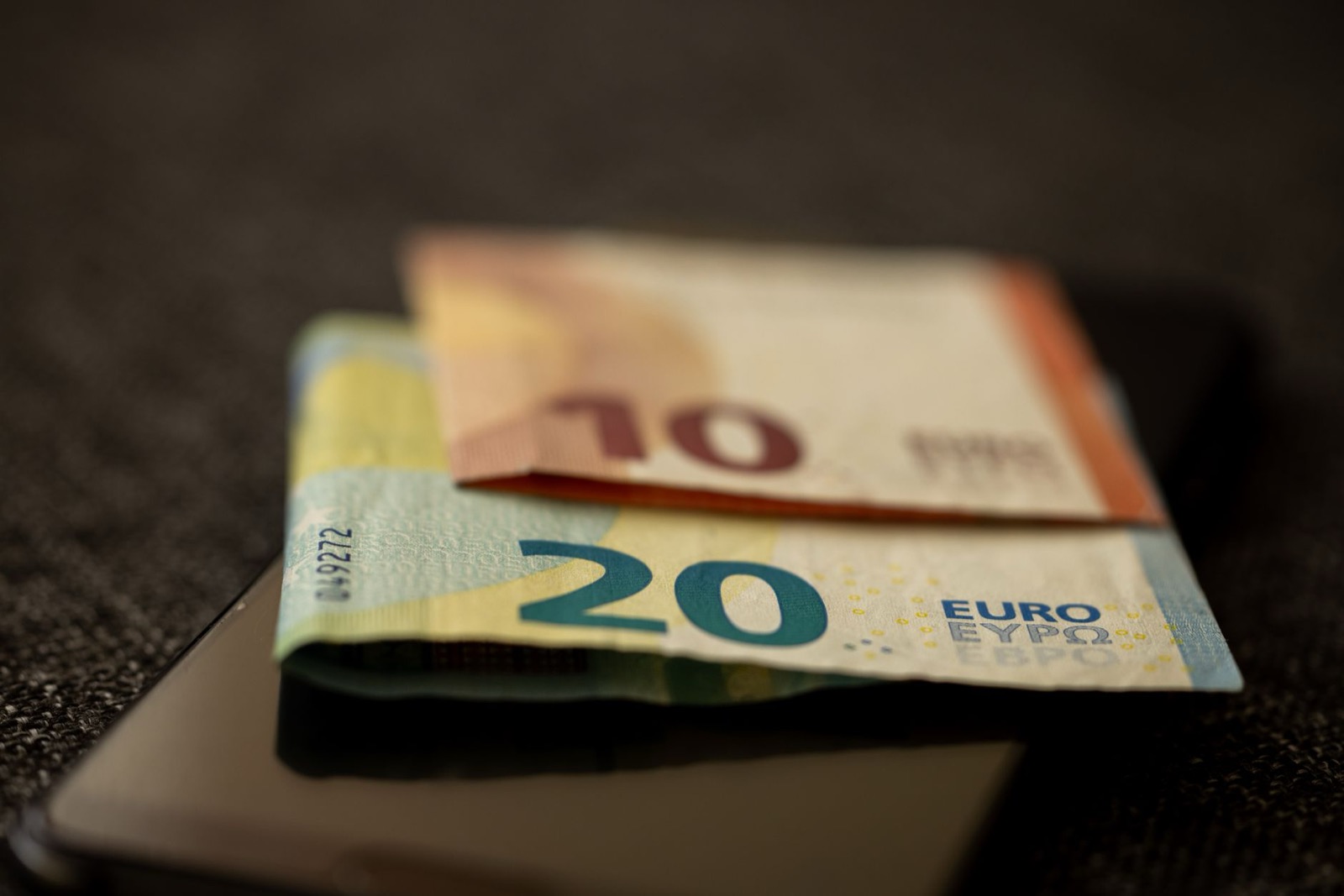 A folded ten and twenty euro note lying on a dark phone on a dark cloth
